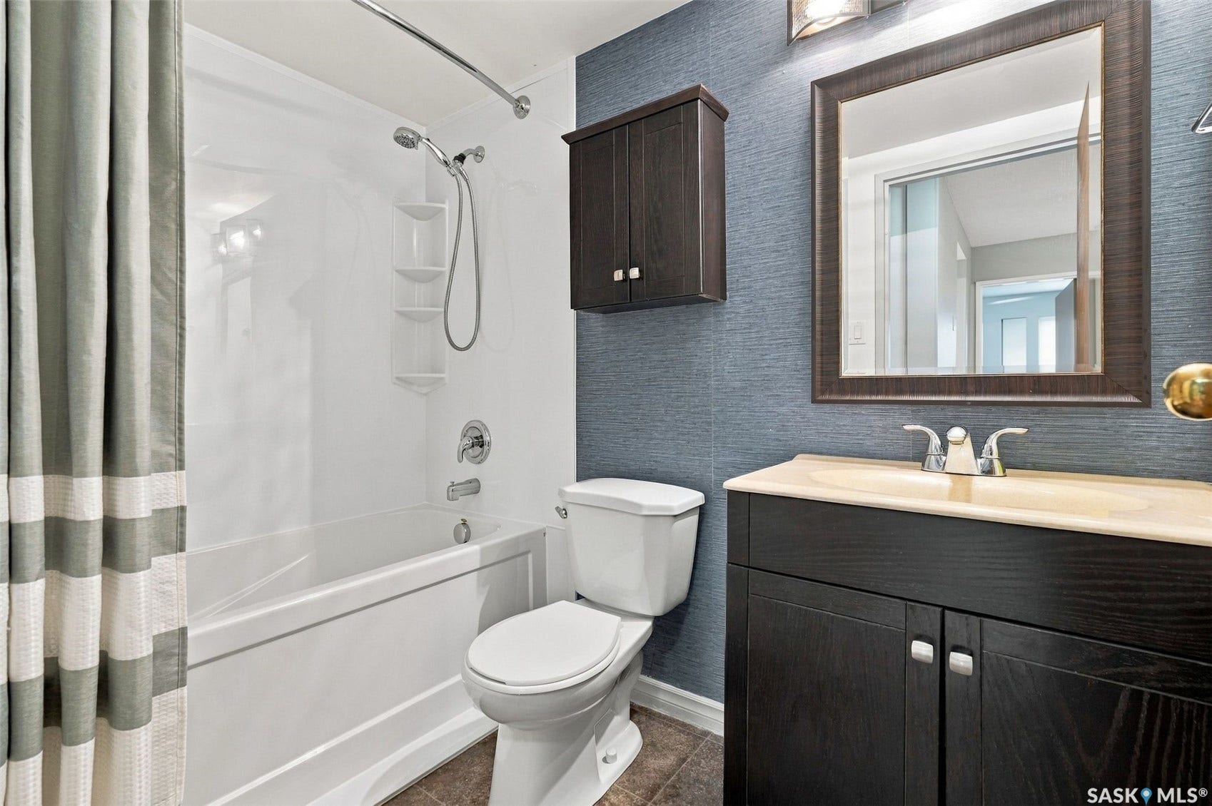 3410 Park Street, #119, Regina SK S4V 2M8 Tub and shower combination with chrome fixtures, dark wood-finish vanity with an integrated sink, framed mirror, wall-mounted storage cabinet, and textured wall covering