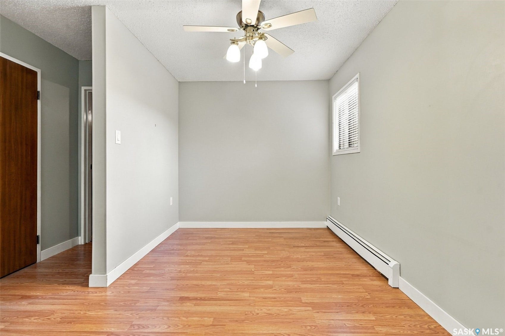 3410 Park Street, #119, Regina SK S4V 2M8 Light gray wall finishes, wood-finish flooring, ceiling fan with integrated lighting, window with horizontal blinds, and a baseboard heater