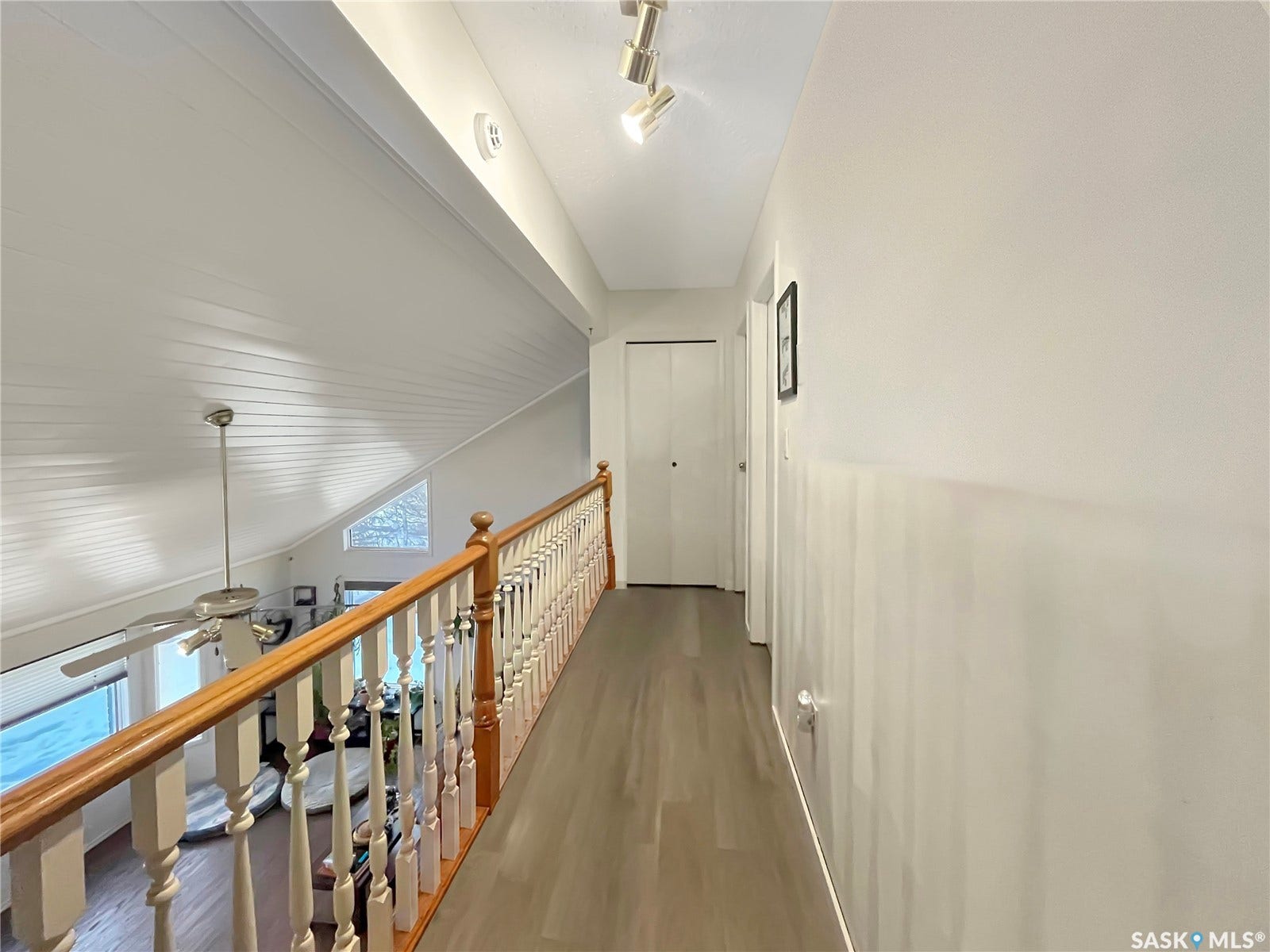 Upper-level walkway featuring wood-finish flooring, track lighting, and a wood handrail with white balusters overlooking a vaulted ceiling
