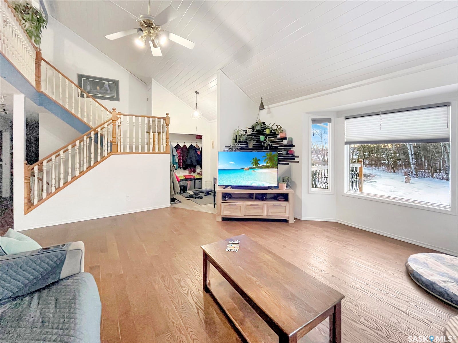 Vaulted ceiling with wood paneling, wood-finish flooring, two-story staircase with wood railing, bay window, and ceiling fan
