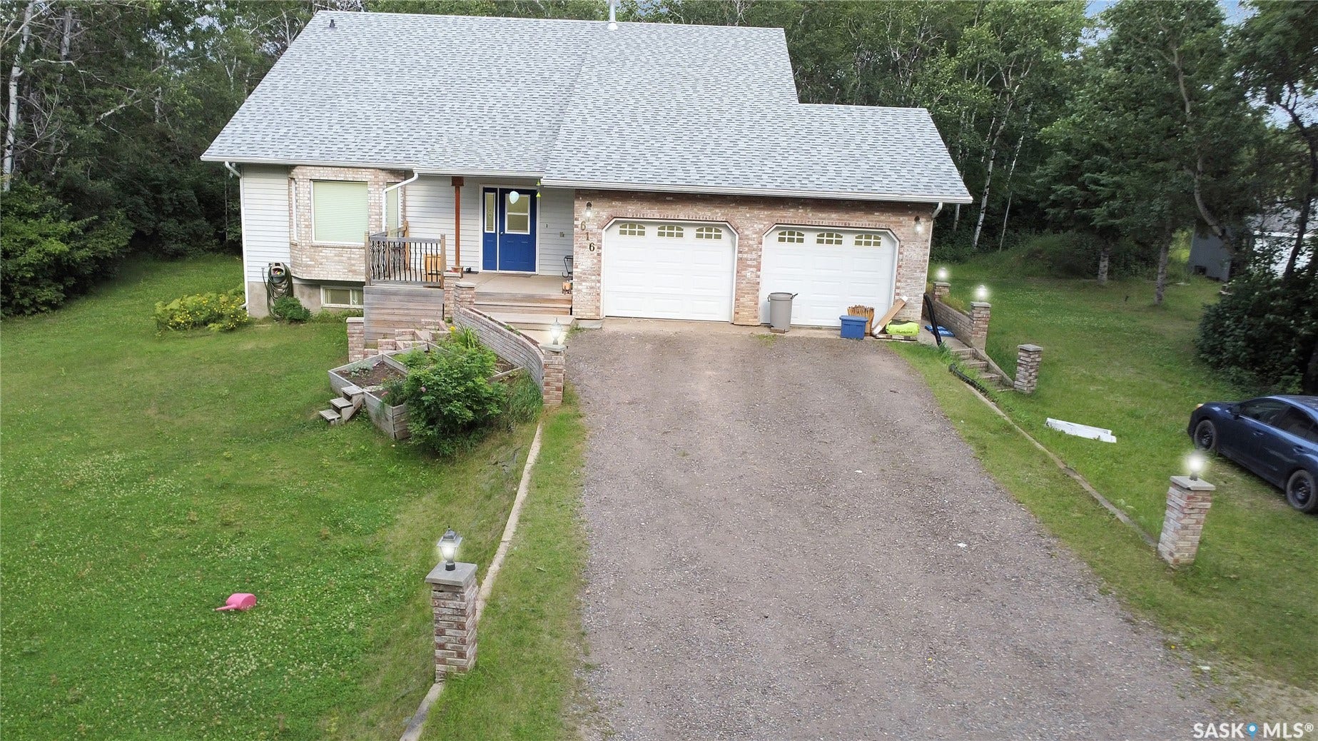 Two-car attached garage, stone facade accents, bay window, front porch with wooden railings, and a gravel driveway