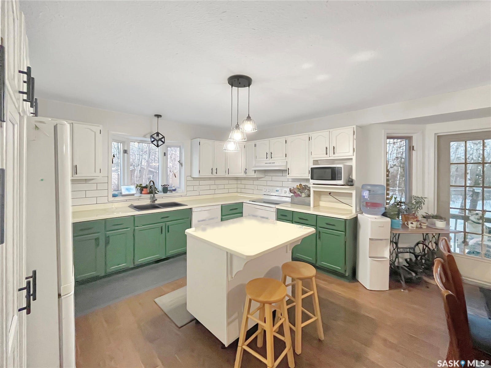 Kitchen featuring wood-finish flooring, white cabinetry, a central island, a white subway tile backsplash, and a double basin sink