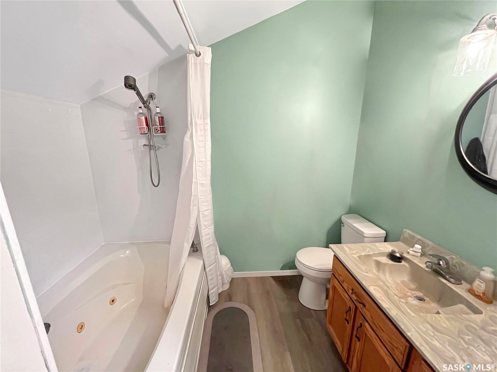 Bathroom featuring a jetted tub, wood-finish flooring, a vanity with integrated sink, and a circular wall mirror