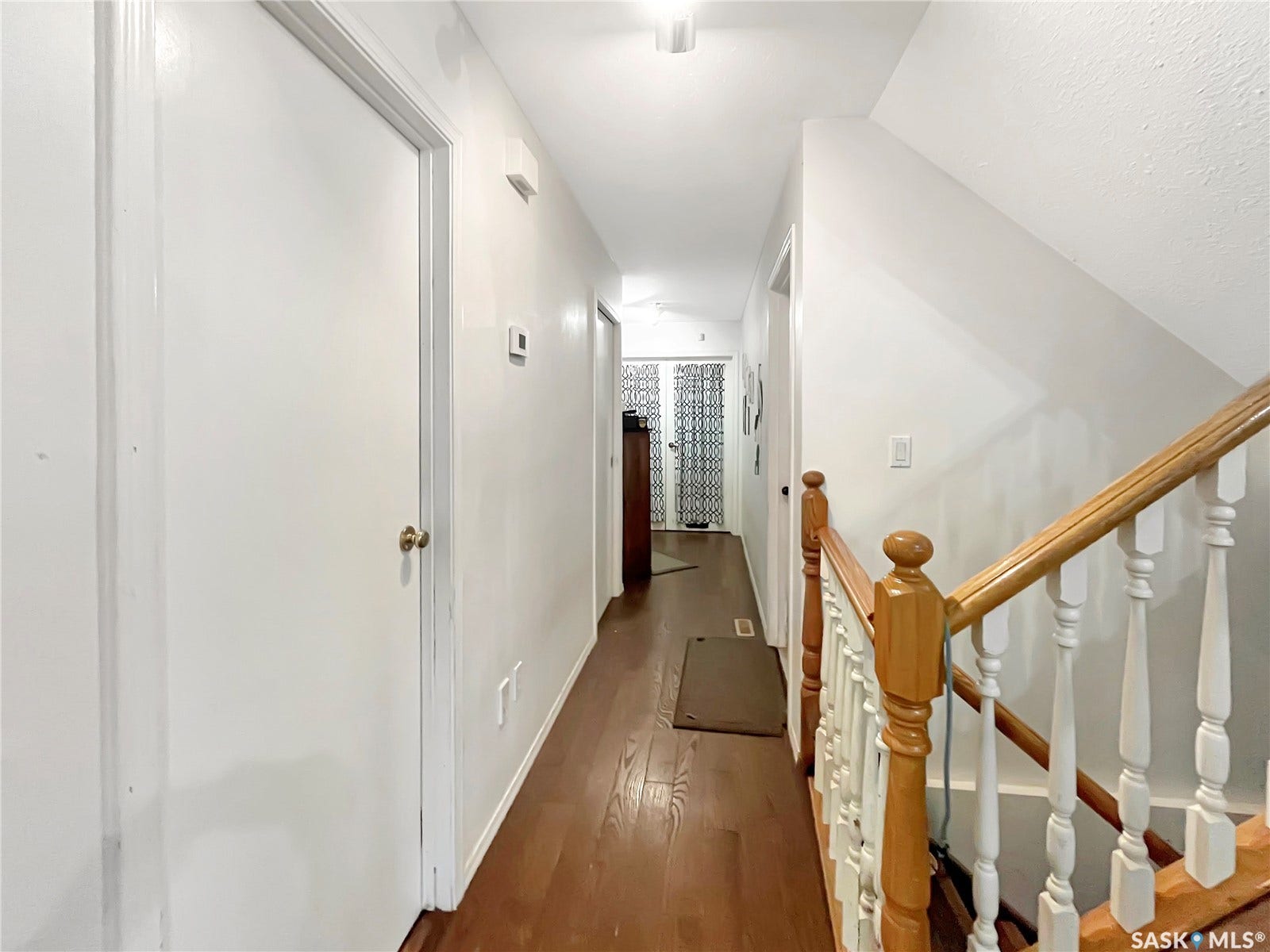 Hallway with wood-finish flooring, white walls, white doors, and a wood and white spindle staircase