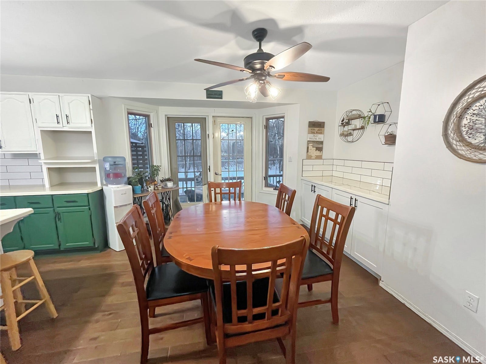 Wood-finish flooring, white upper cabinetry, green base cabinetry, white subway tile backsplash, and a ceiling fan with light fixture