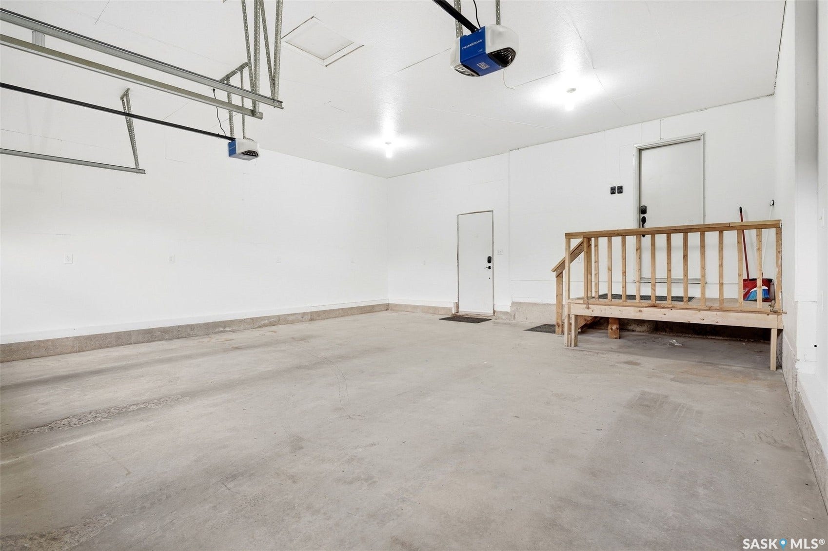 Spacious garage with concrete flooring, white walls, two overhead garage door openers, and a built-in wooden stair platform