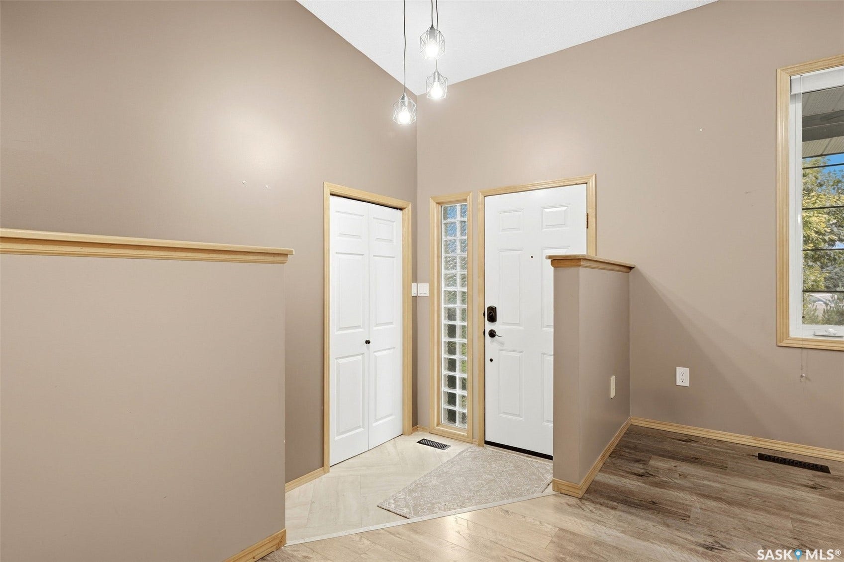 Vaulted ceiling with suspended lighting, a paneled entry door with sidelight, a bi-fold closet door, and wood-finish flooring