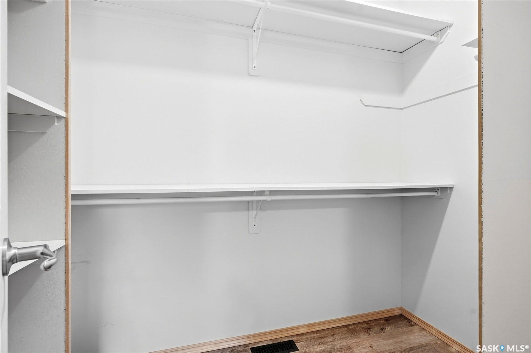 White walls and wood-finish flooring in a closet space with multiple shelving units and hanging rods