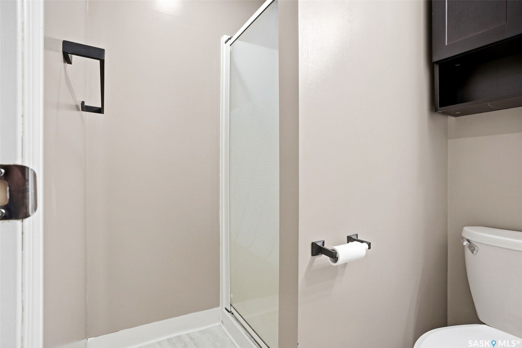 Glass-enclosed shower with a matte black towel hook, white toilet, and dark wood-finish wall-mounted cabinetry