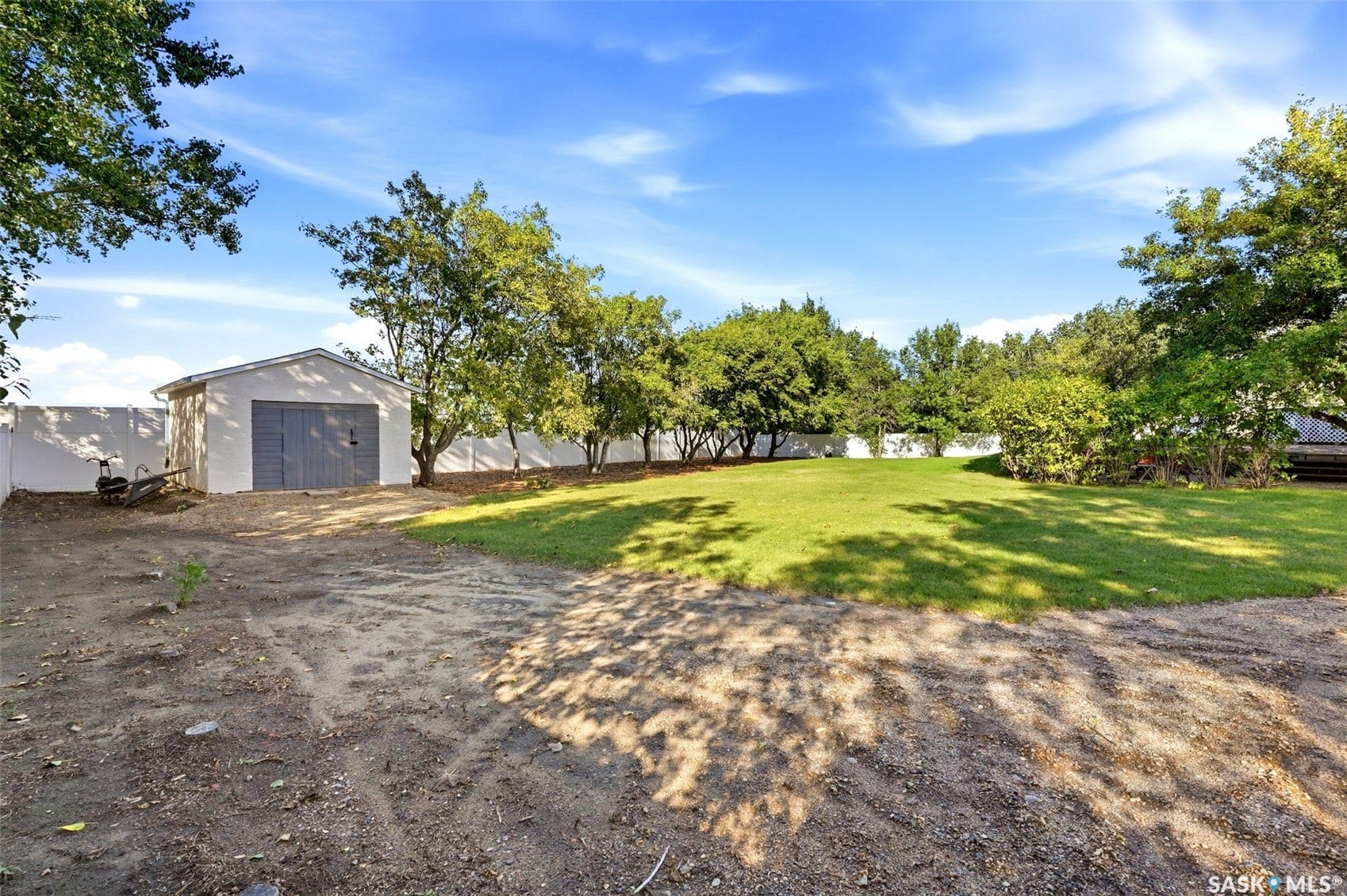 Detached storage shed with a roll-up door, expansive lawn area, mature trees, and a perimeter fence