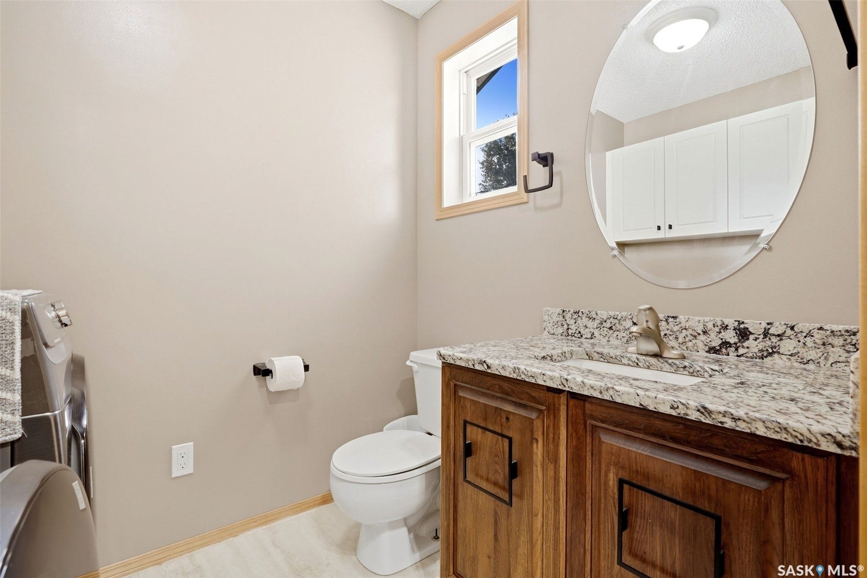 Vanity with stone countertop, undermount sink, wood-finish cabinetry, and an oval mirror