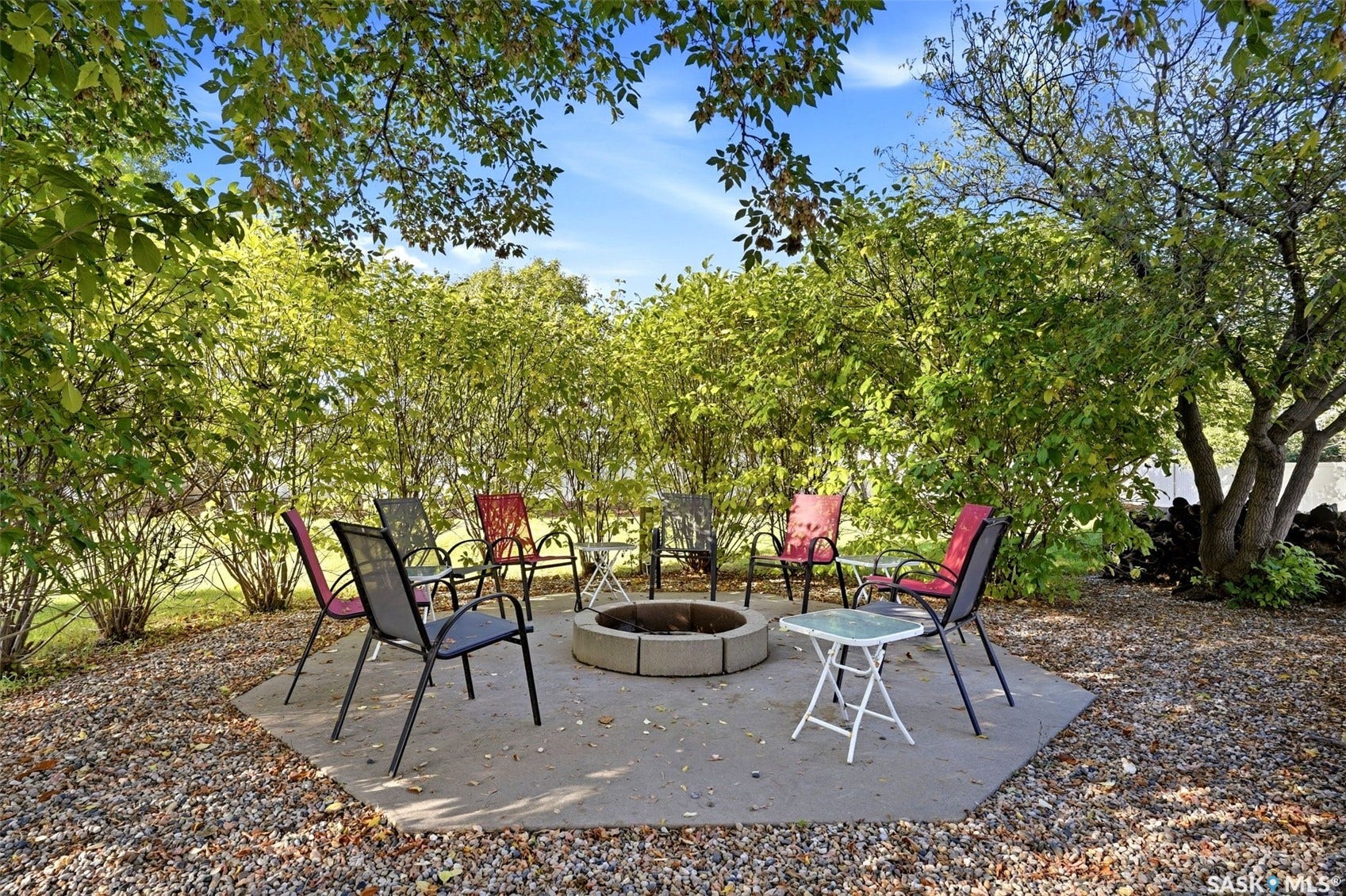 Hexagonal concrete patio with built-in fire pit, surrounded by mature trees and lush shrubbery