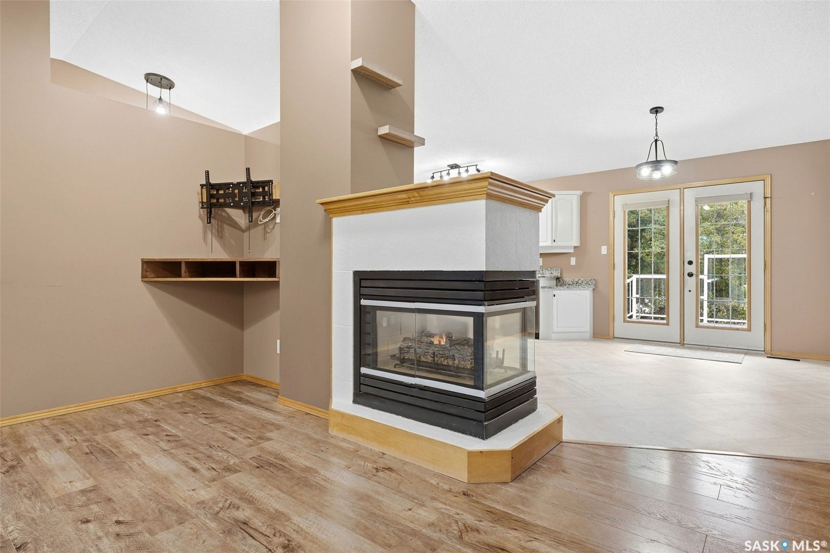 Central corner fireplace with a wood mantel, wood-finish flooring, built-in shelving, white cabinetry, and double French doors