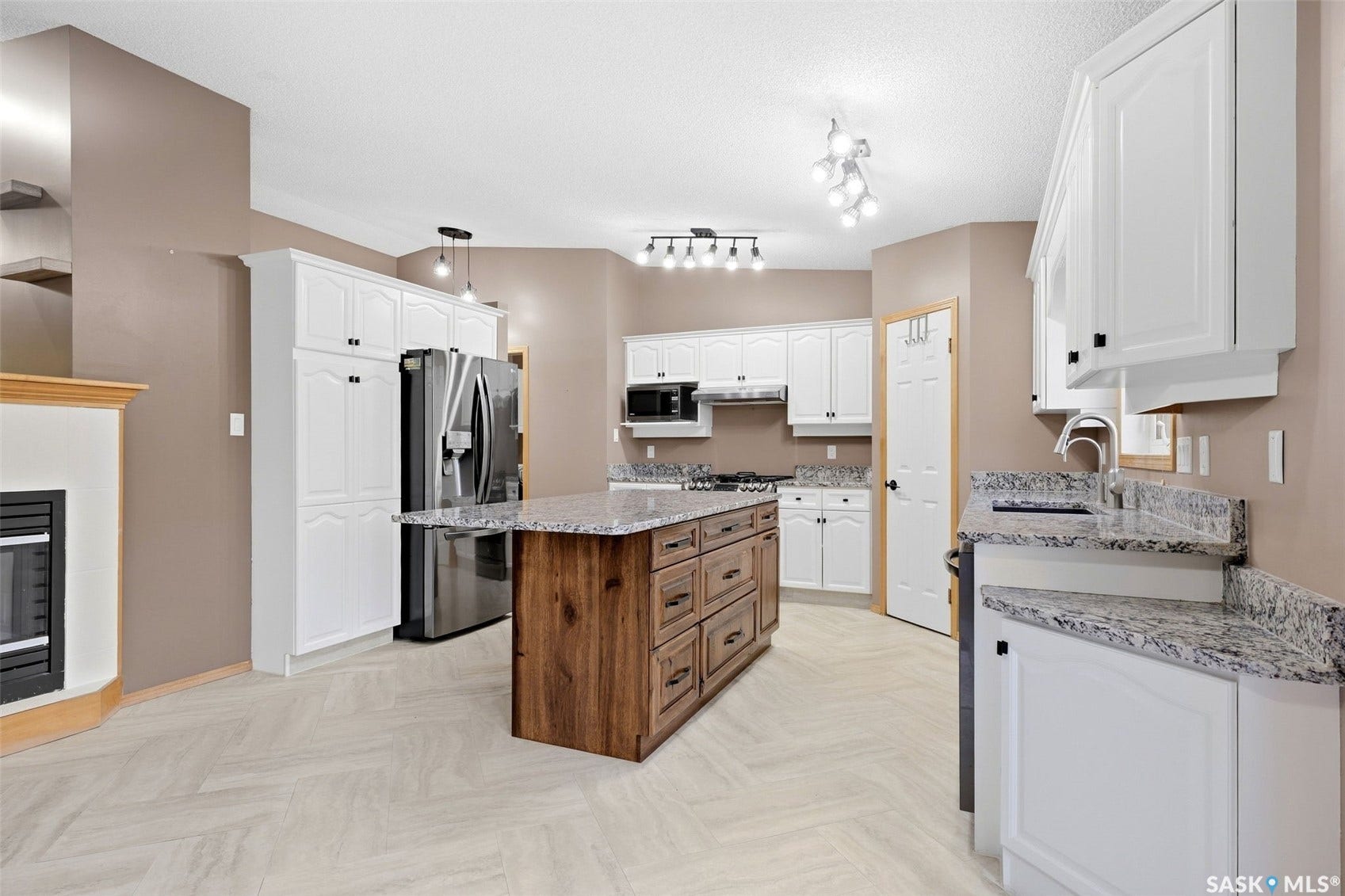 Spacious kitchen with wood-finish island, white cabinetry, integrated stainless steel appliances, speckled countertops, and light-toned flooring