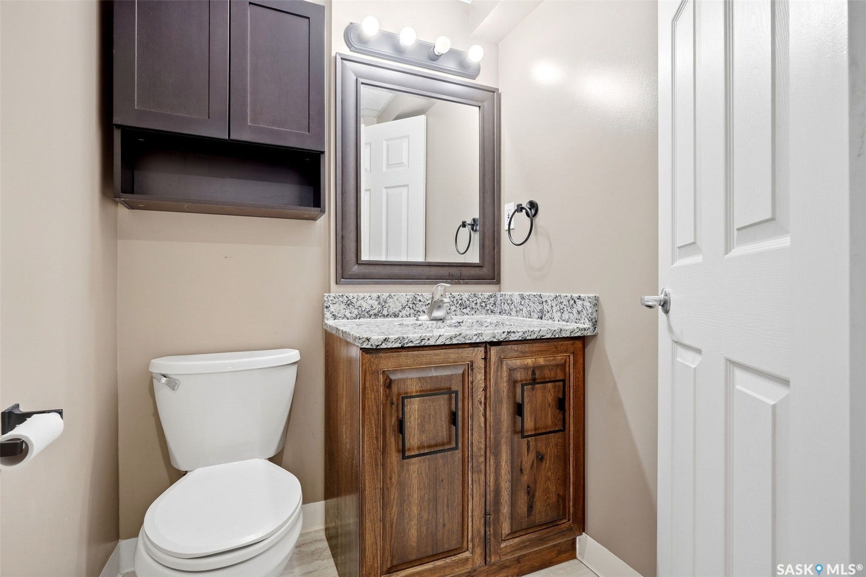 Vanity with granite countertop, wood-finish cabinetry, and framed mirror