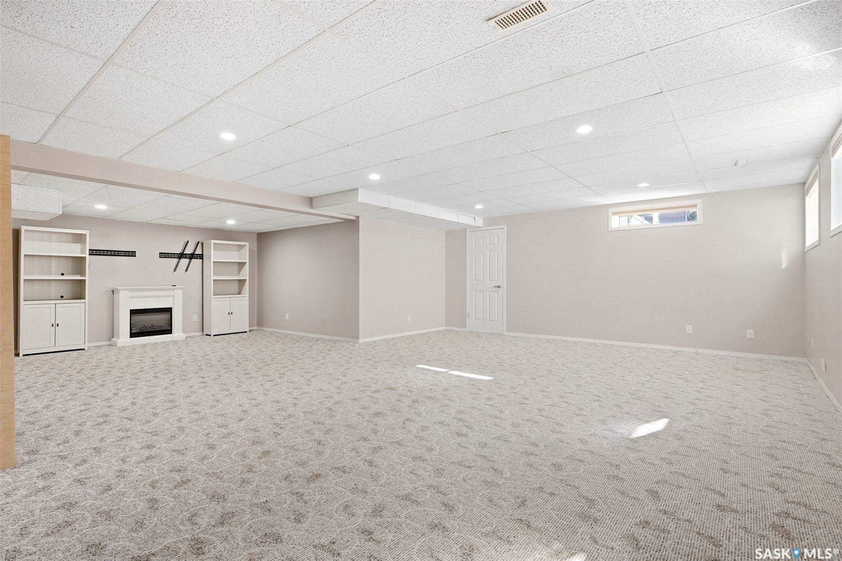 Expansive carpeted room featuring a white fireplace with a mantel, built-in shelving units, recessed lighting, and multiple windows