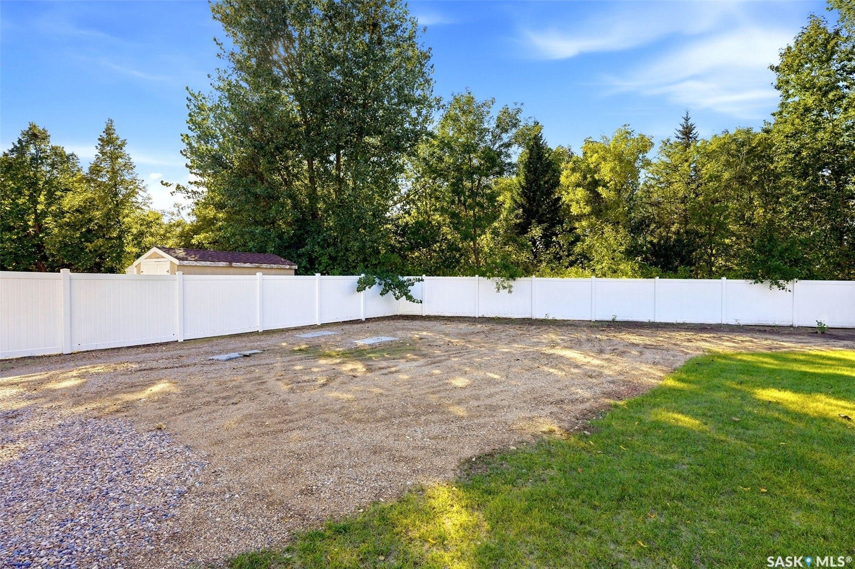 Expansive outdoor area featuring a white privacy fence, gravel, and a grass section