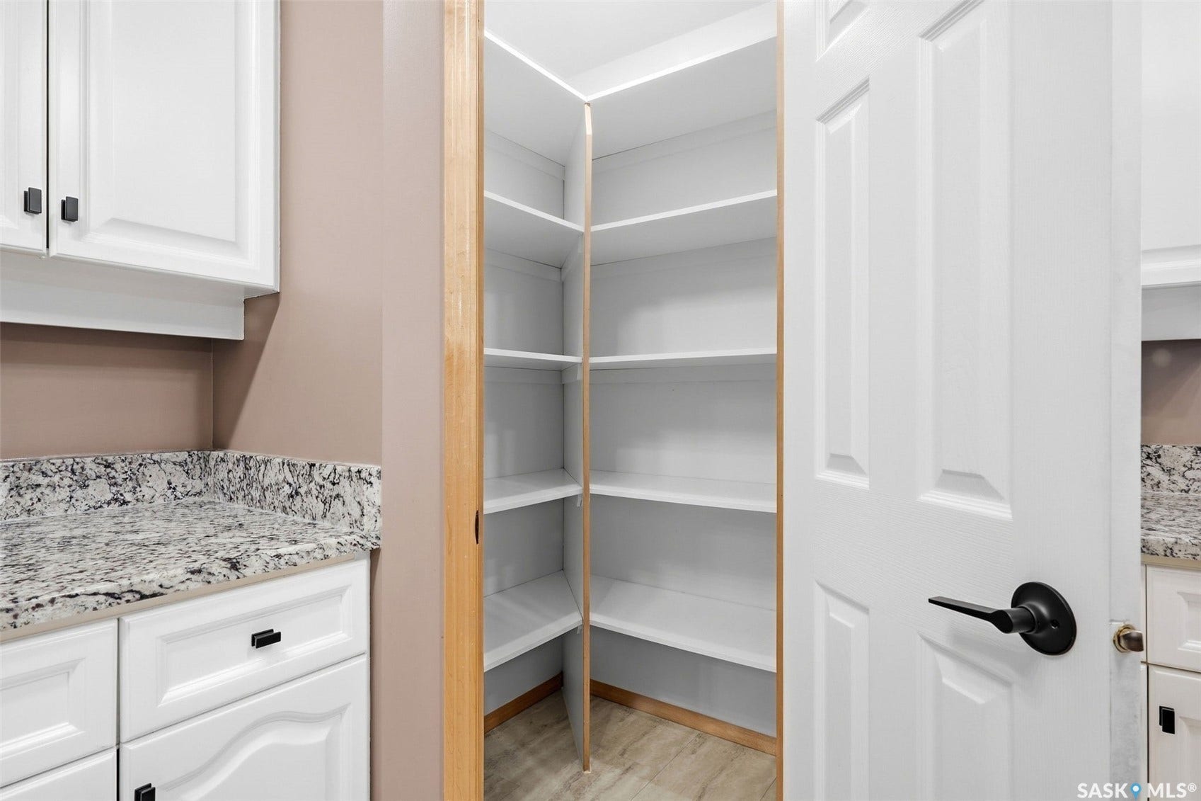 Built-in pantry with ample shelving, white cabinetry, granite-style countertops, and matte black hardware