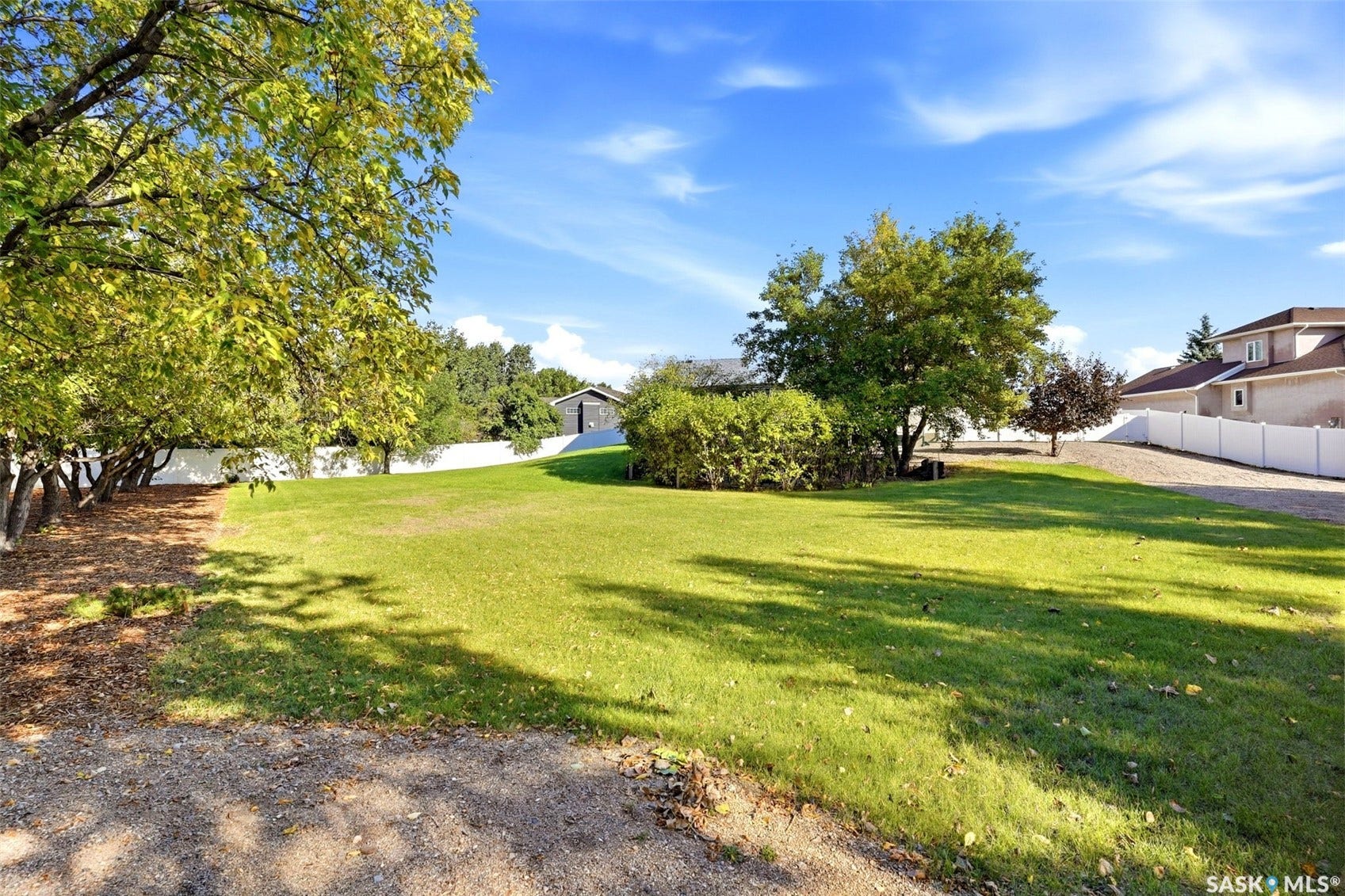 Expansive grassy lawn with mature trees and a white privacy fence