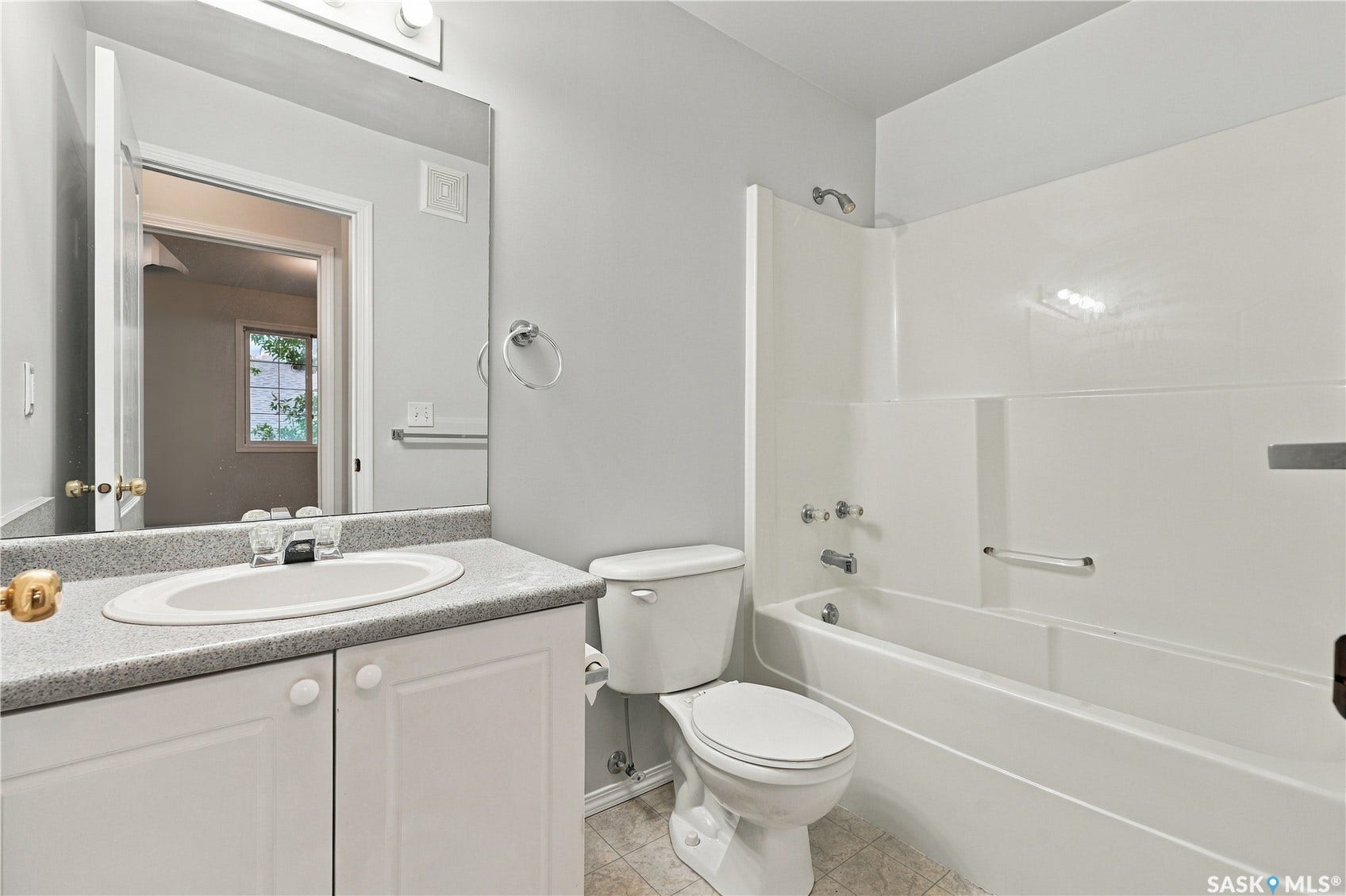 Vanity with an integrated sink and speckled countertop, white cabinetry, a full-width mirror, and a white tub with an integrated shower