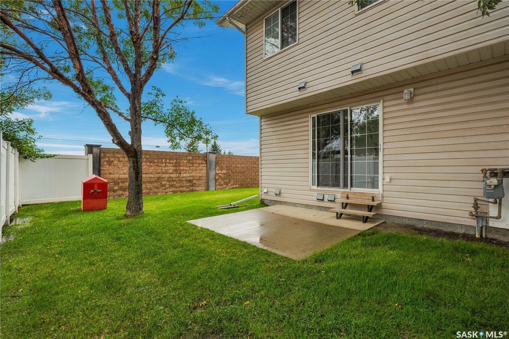 Expansive backyard featuring a manicured lawn, concrete patio, and mature tree
