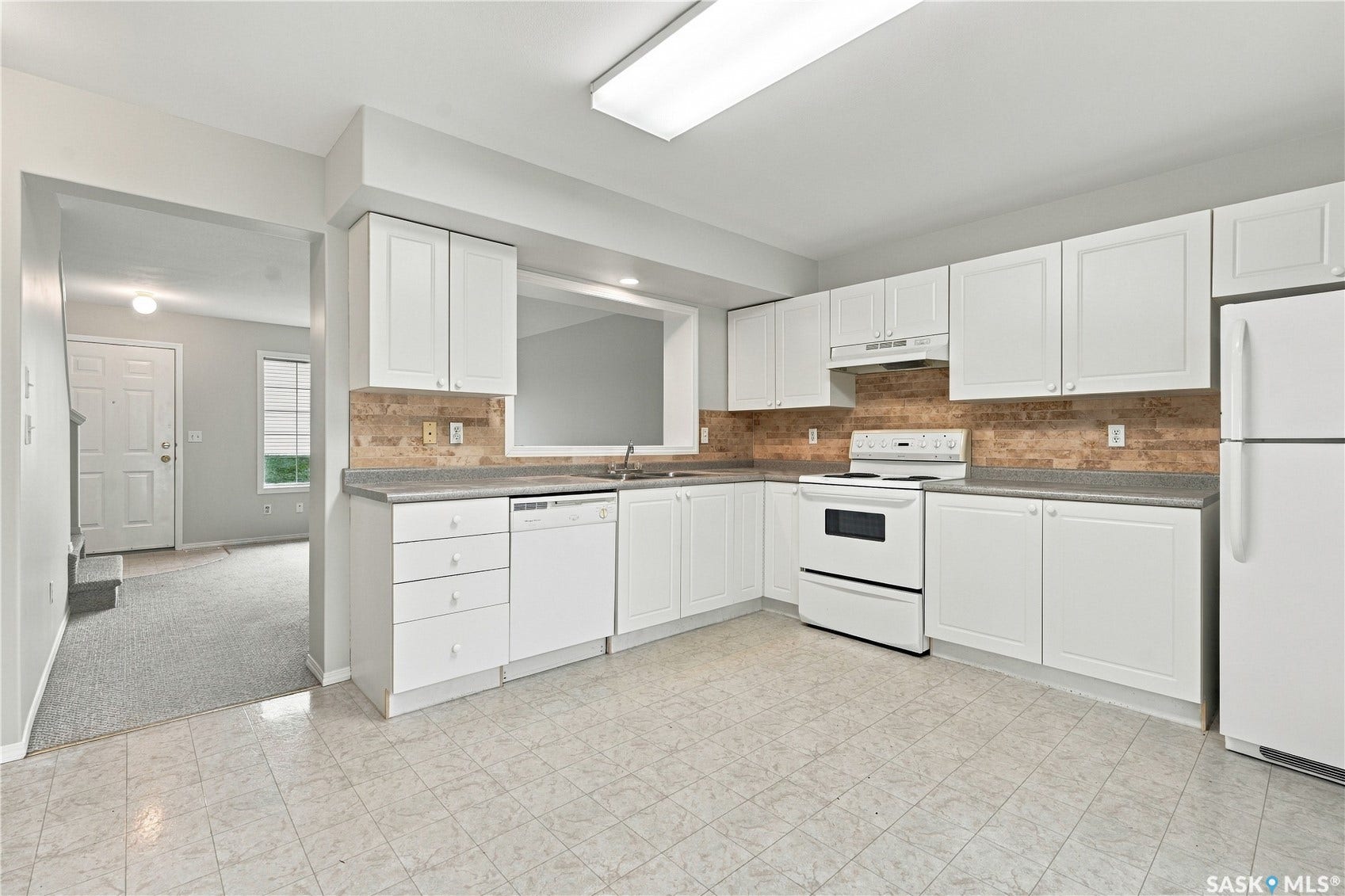 White cabinetry with brushed nickel hardware, laminate countertops, a tile backsplash, kitchen appliances, and tile flooring