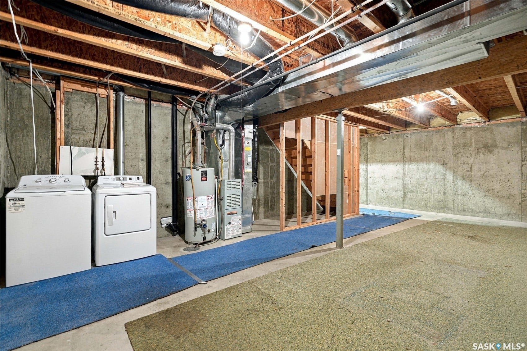 Unfinished basement space with concrete walls, exposed ceiling joists, laundry appliances, a water heater, and HVAC system