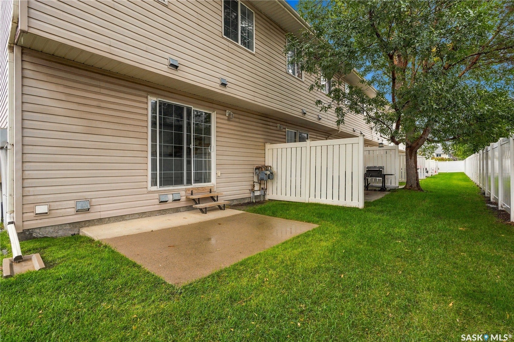 Exterior features include horizontal siding, a concrete patio, a sliding glass door, a privacy fence, and a mature tree
