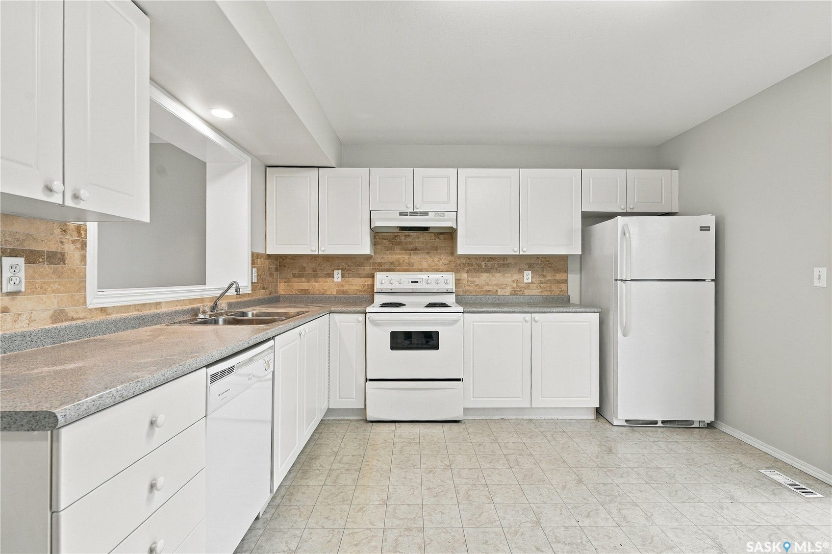 Kitchen featuring white cabinetry, stone-look countertops, a tile backsplash, and a window above the double-basin sink