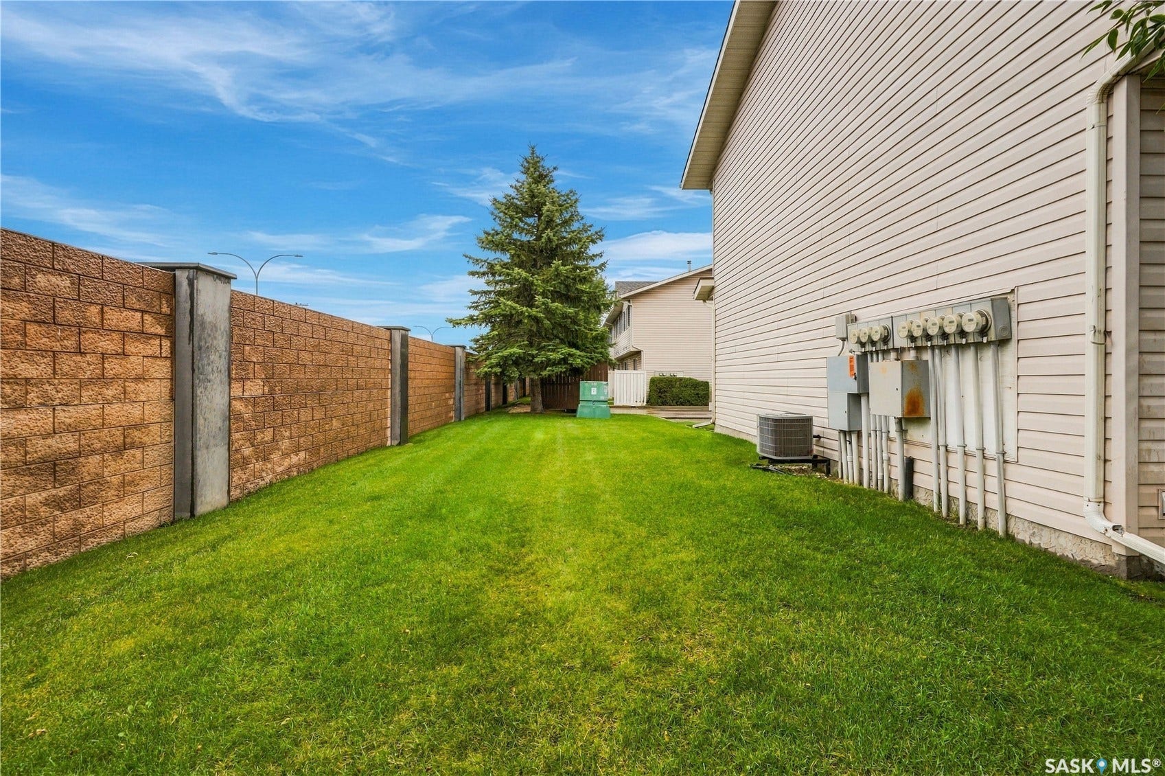Expansive side yard featuring a manicured lawn, a tall evergreen tree, and a brick-finish retaining wall