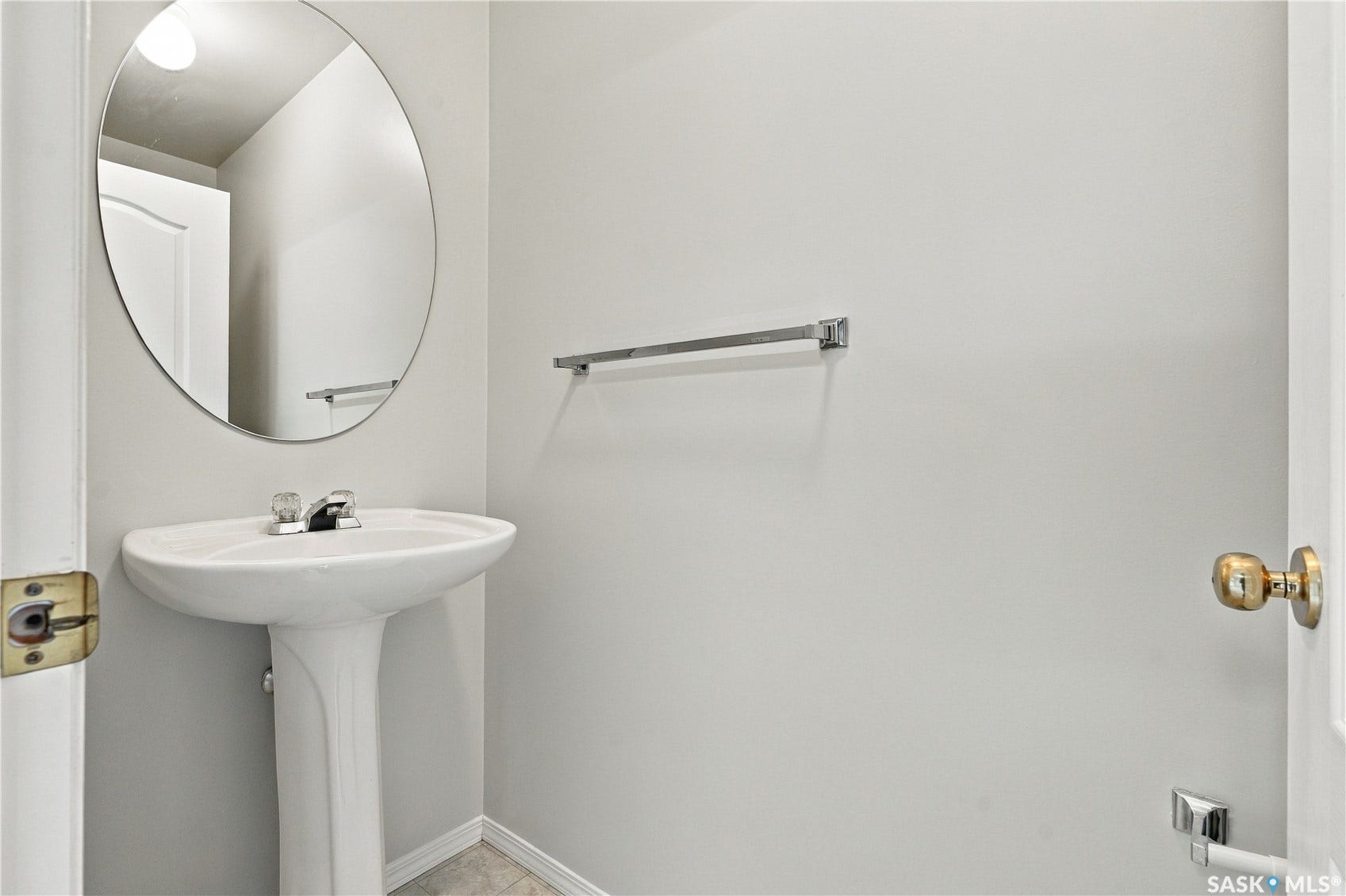 Pedestal sink with chrome-finish faucet, circular wall-mounted mirror, and wall-mounted towel bar