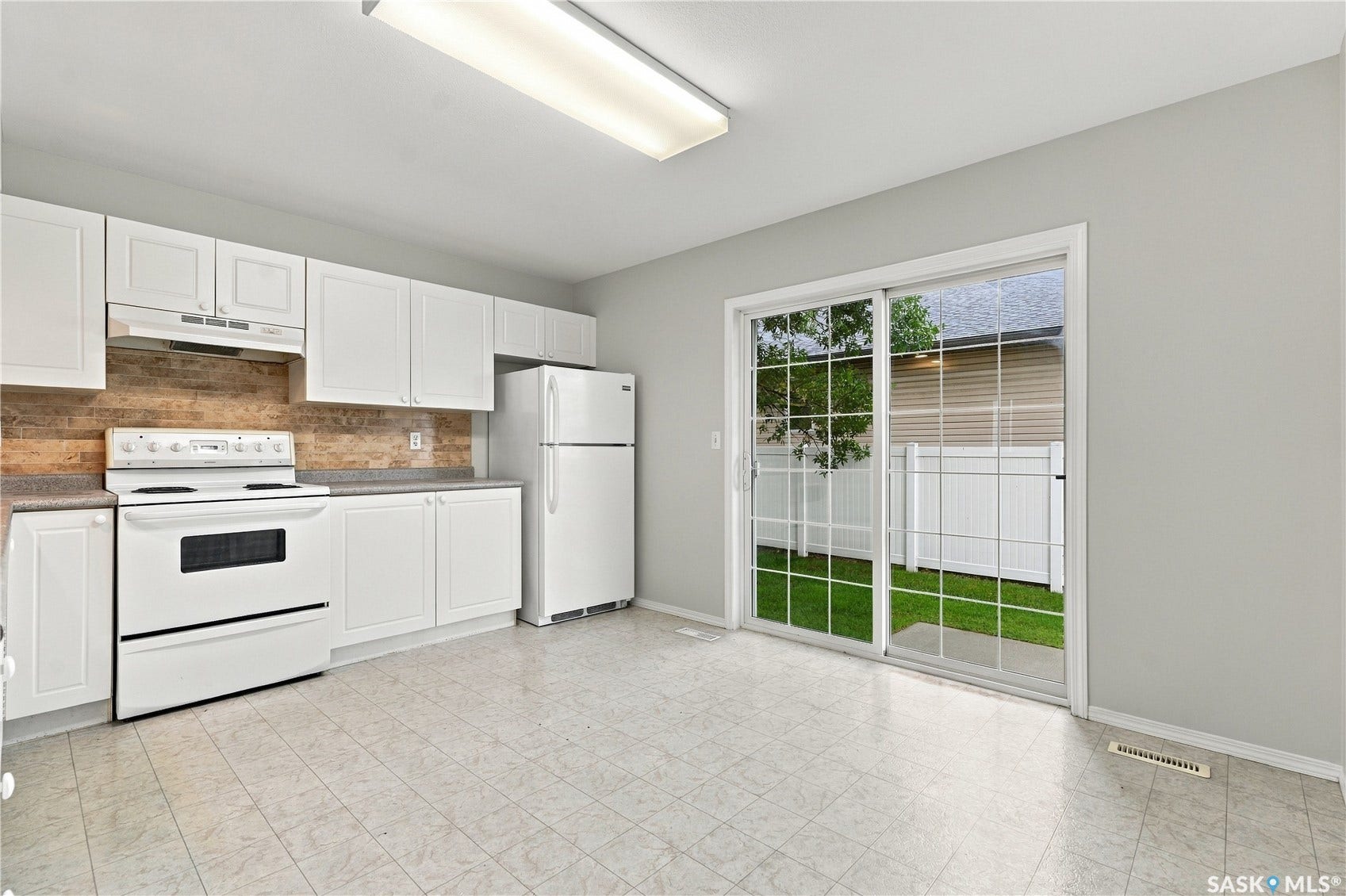 White kitchen cabinetry with a wood-finish backsplash and light-toned countertops