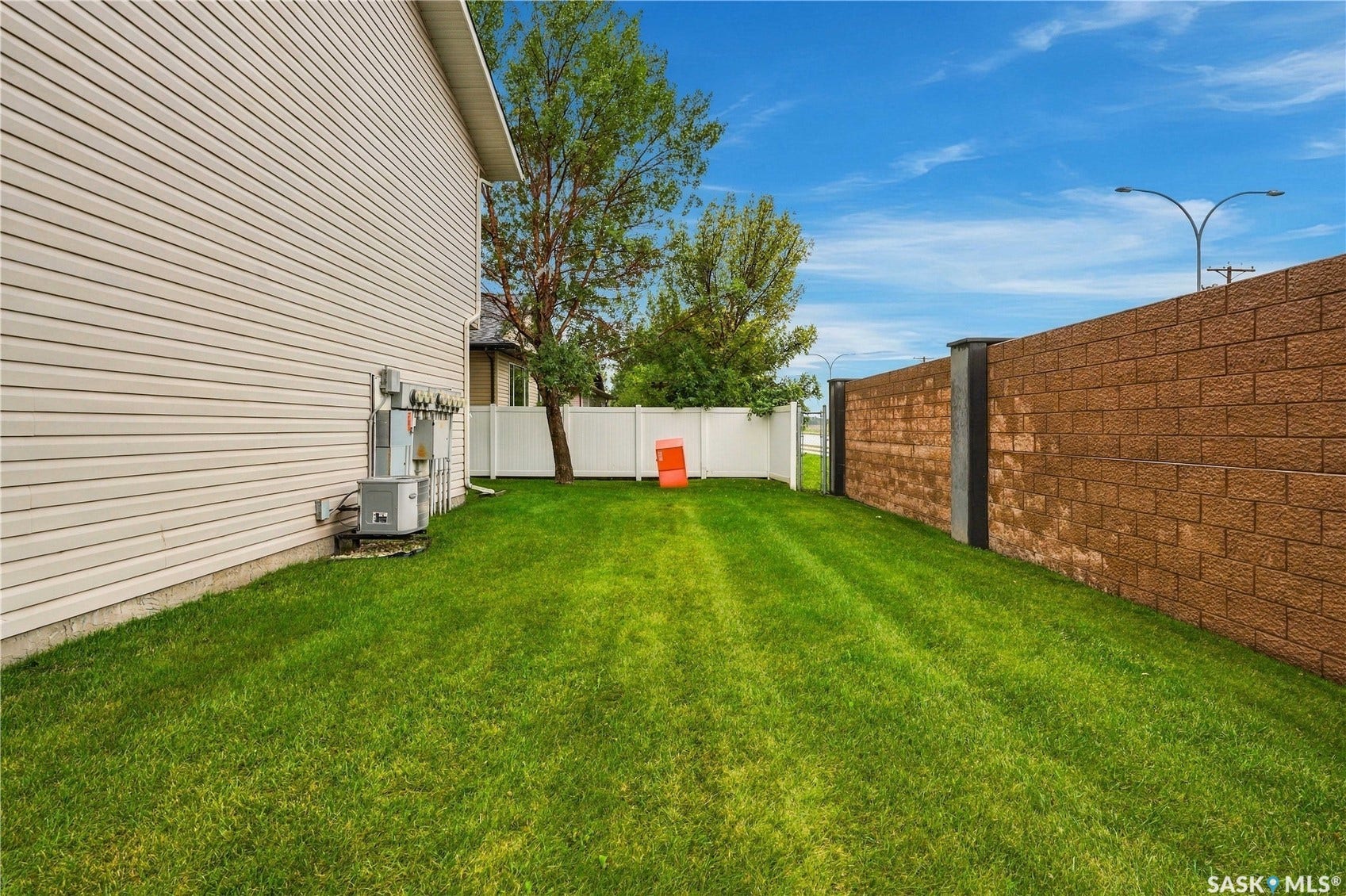 Expansive grassy area featuring a white vinyl privacy fence and a tall brick wall