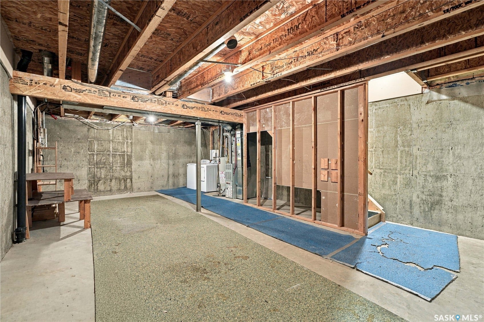 Unfinished basement with concrete walls, exposed wood ceiling joists, and a partial wood-framed partition