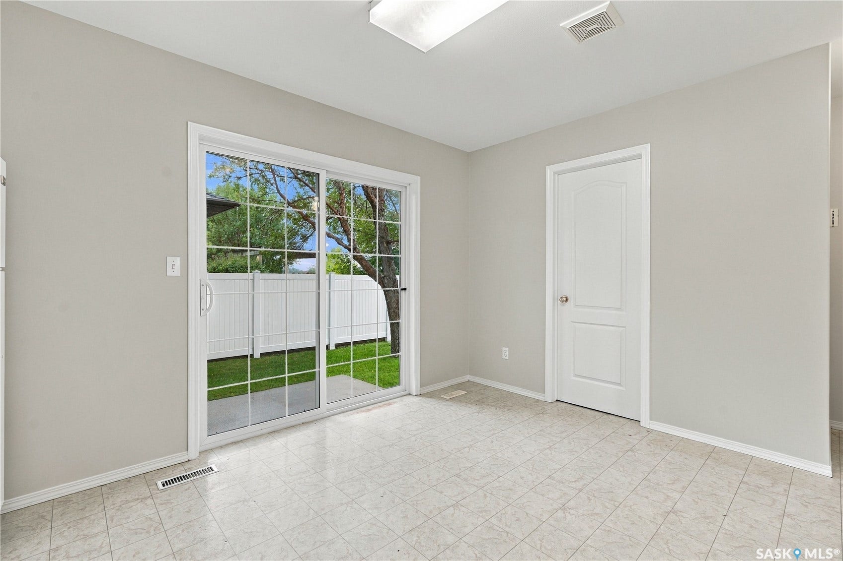 Sliding glass door to exterior patio and fenced yard, light-toned tile flooring, light-colored walls, ceiling-mounted lighting, and white paneled interior door