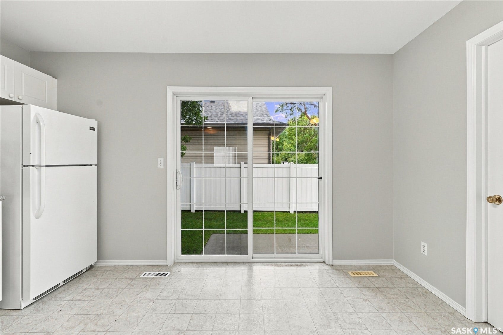Sliding glass door to the exterior, white upper cabinetry, white refrigerator, and tile flooring
