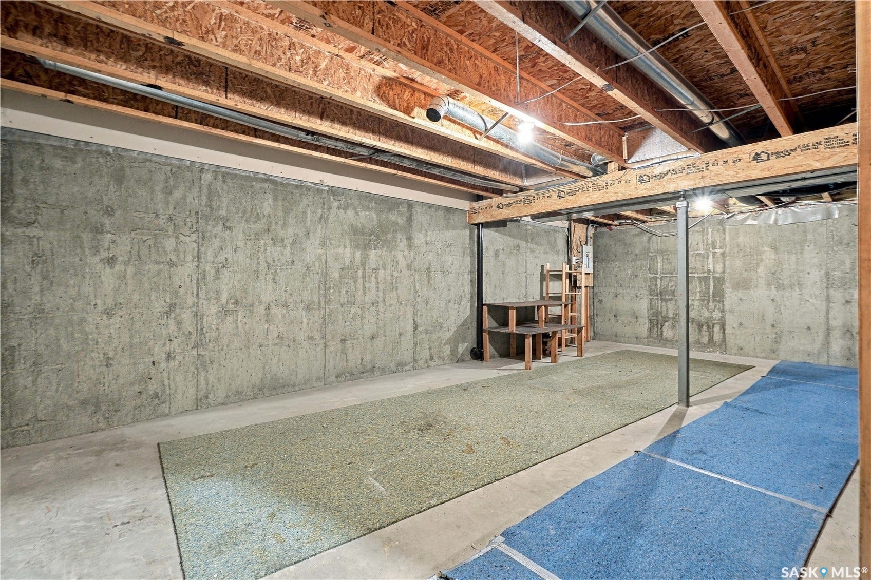 Unfinished lower level with concrete walls, exposed wood ceiling joists, and overhead lighting
