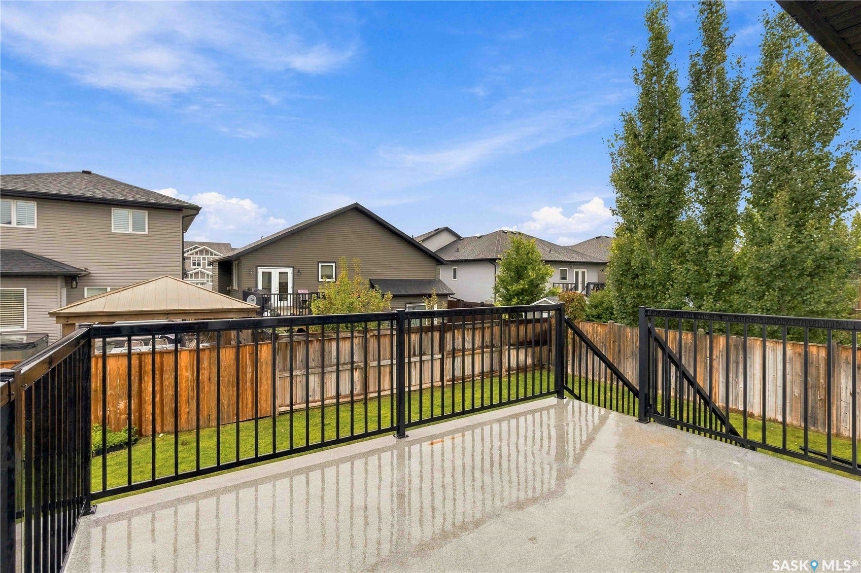 Wooden Deck featuring black metal railings and a fully fenced backyard with underground sprinkler lawn