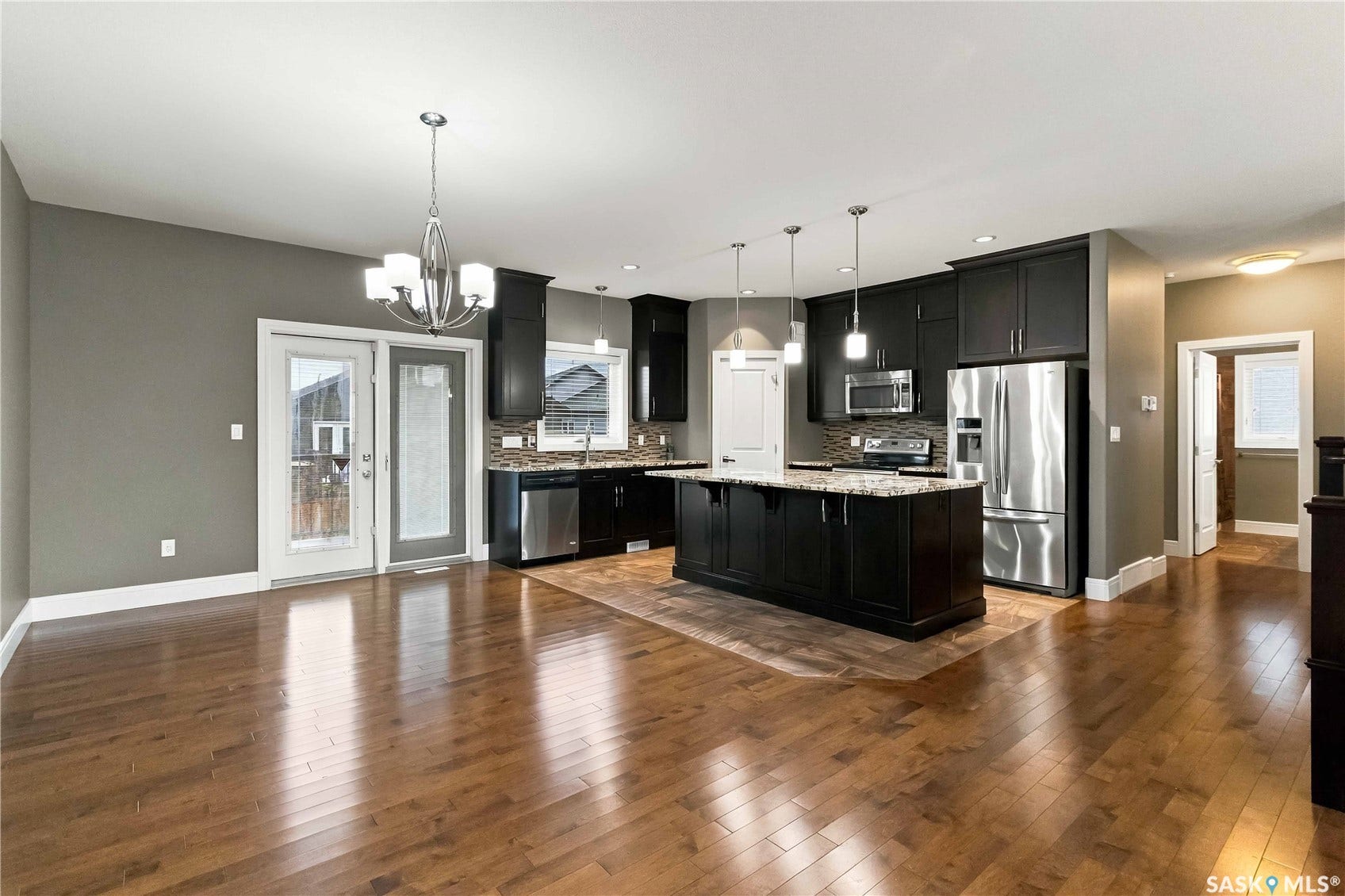 Open-concept living area with wood-finish flooring, dark cabinetry, stainless steel appliances, a kitchen island with seating, and glass panel patio doors