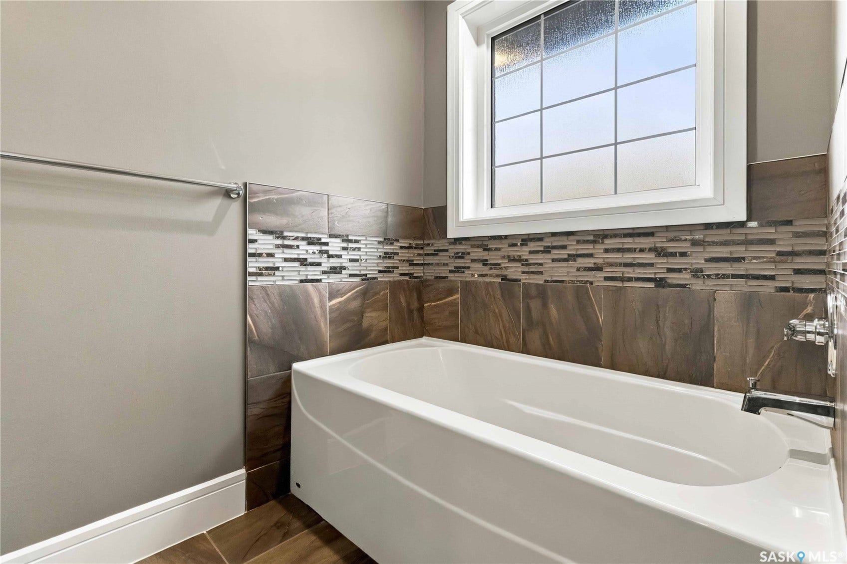 Bathtub with a chrome faucet, large-format wall tiles, and a decorative mosaic tile band