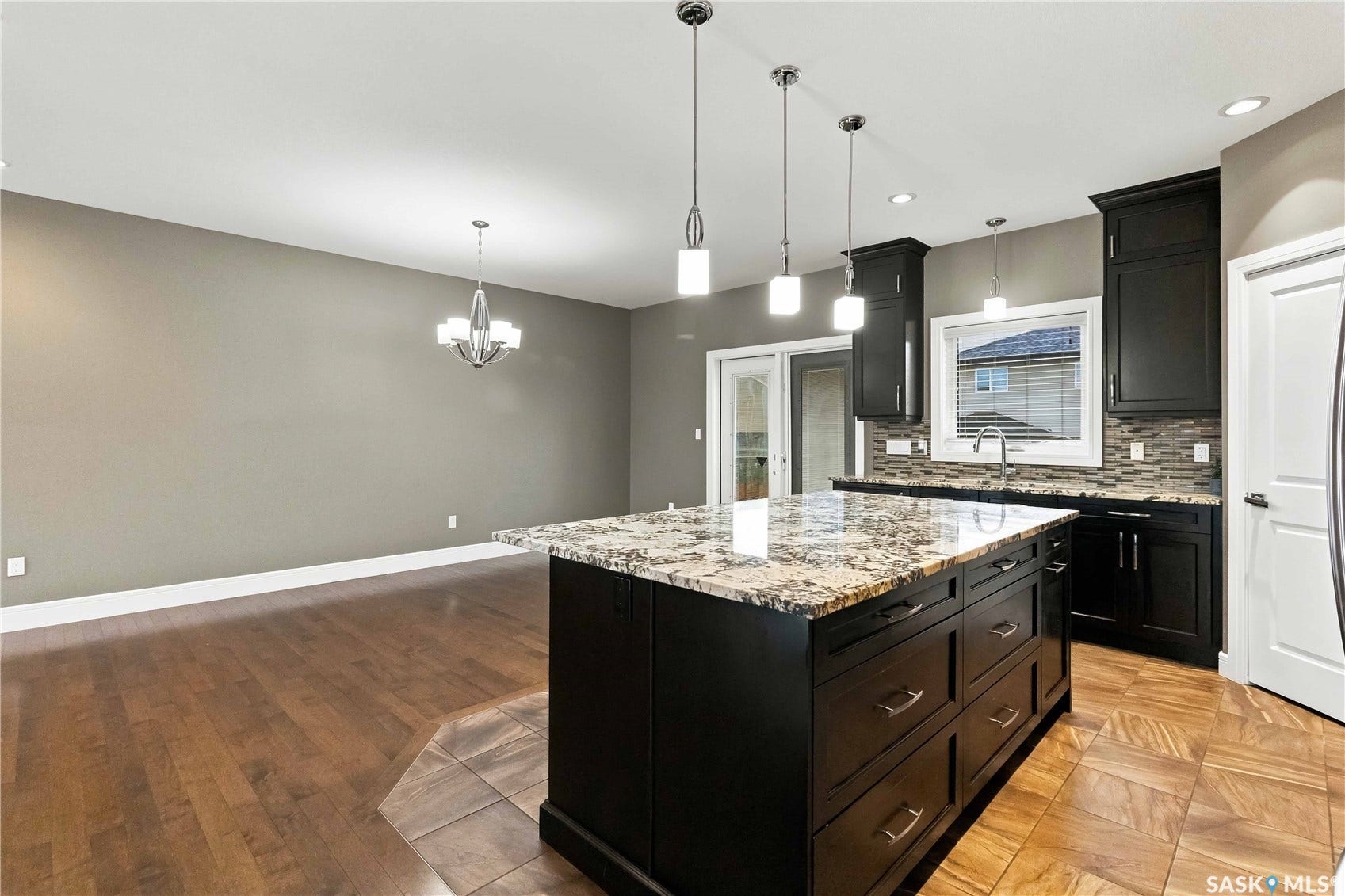 Kitchen with dark cabinetry, stone countertops, a tile backsplash, and an island with pendant lighting