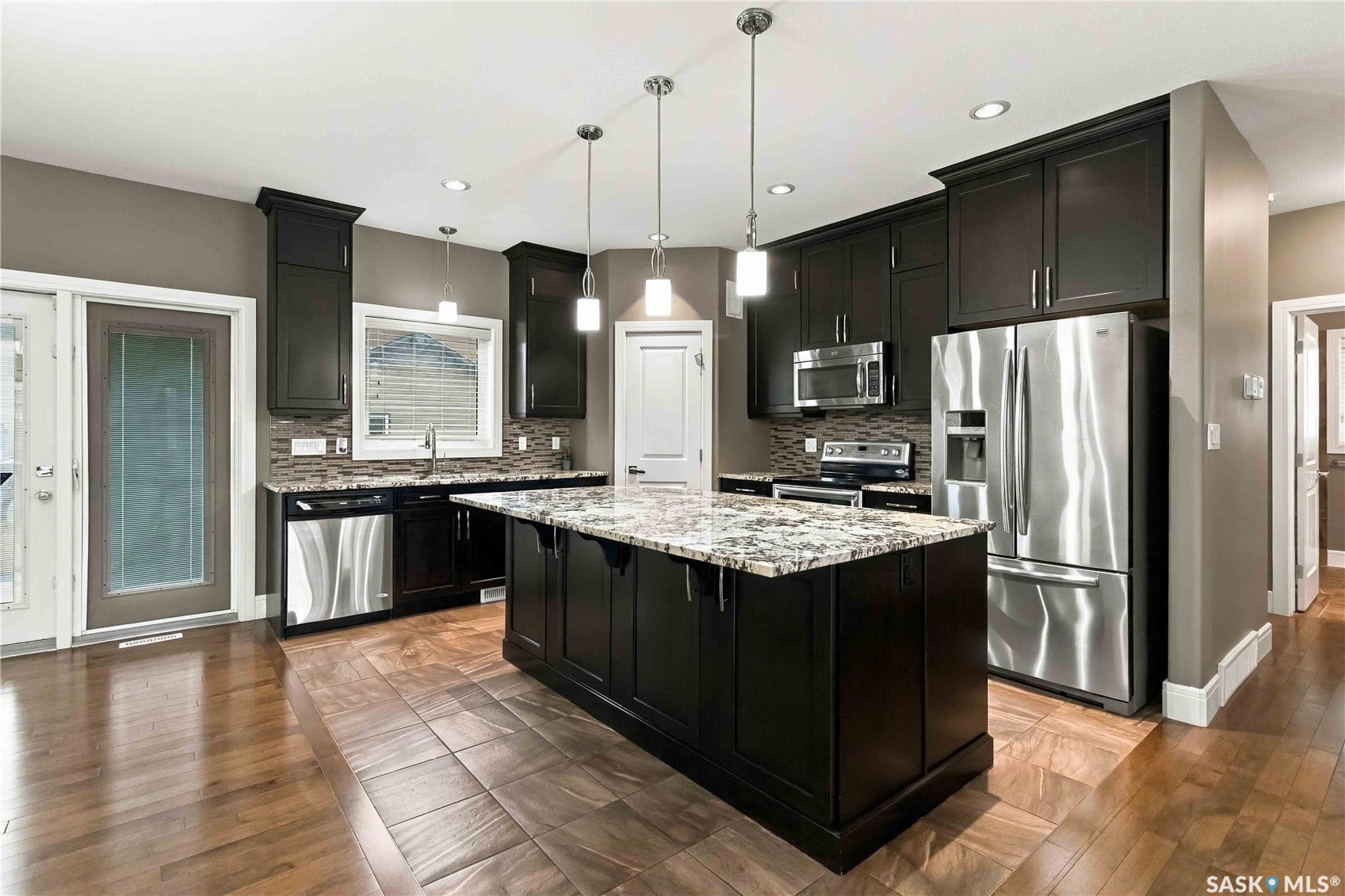 Expansive kitchen featuring dark wood cabinetry, stainless steel appliances, a central island with a light-toned countertop, and recessed lighting