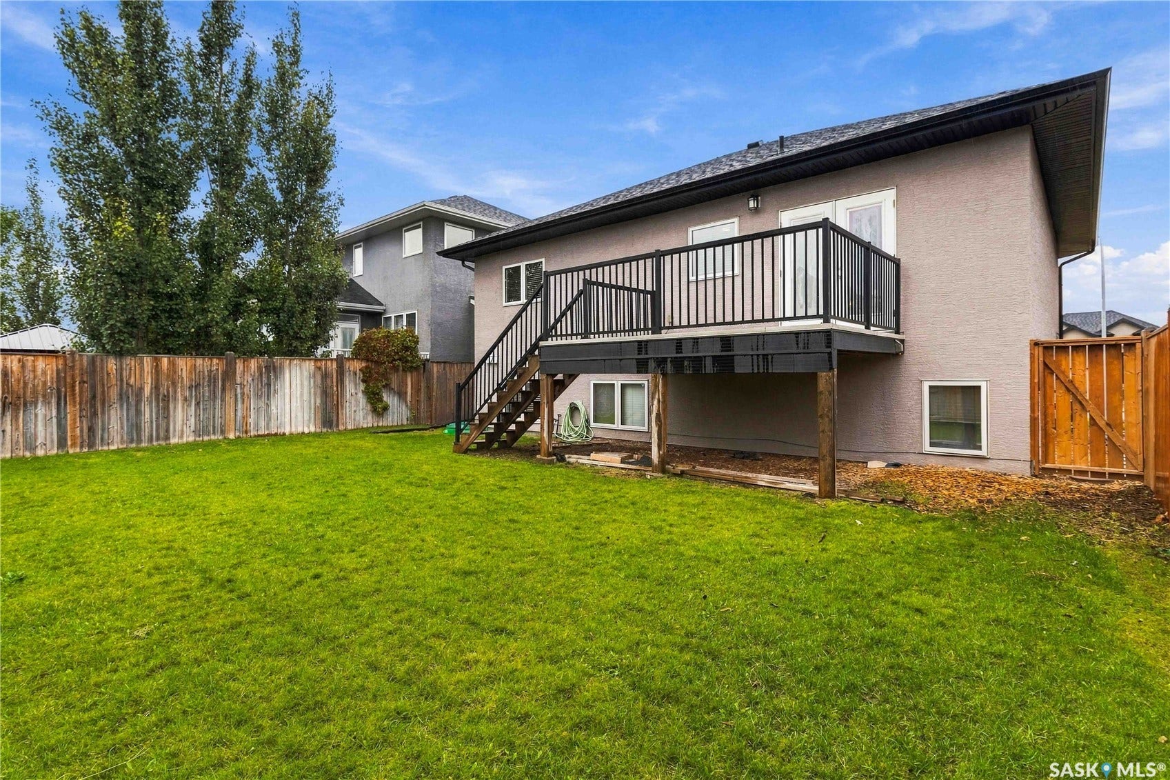 Expansive backyard featuring a manicured lawn, wood fencing, and a raised exterior deck with black railings