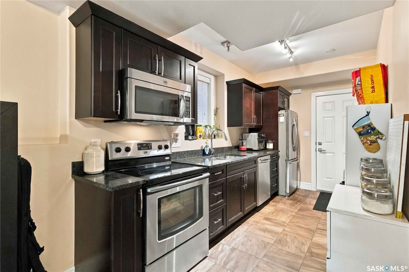 Kitchen featuring dark wood-finish cabinetry, stainless steel appliances, dark stone countertops, and wood-look tile flooring