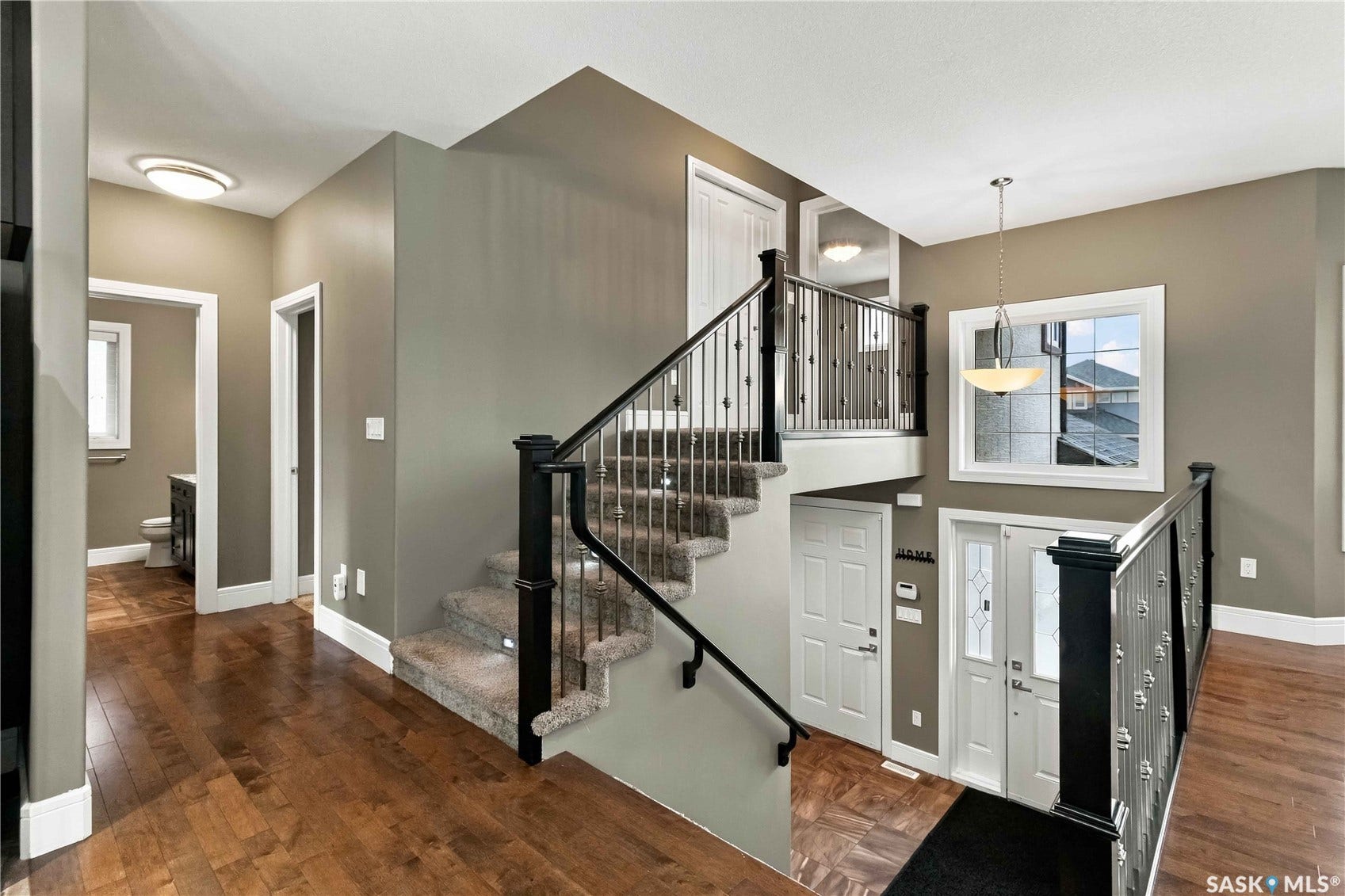 Hardwood flooring, carpeted stairs, wrought iron balusters, white trim, and a decorative pendant light fixture