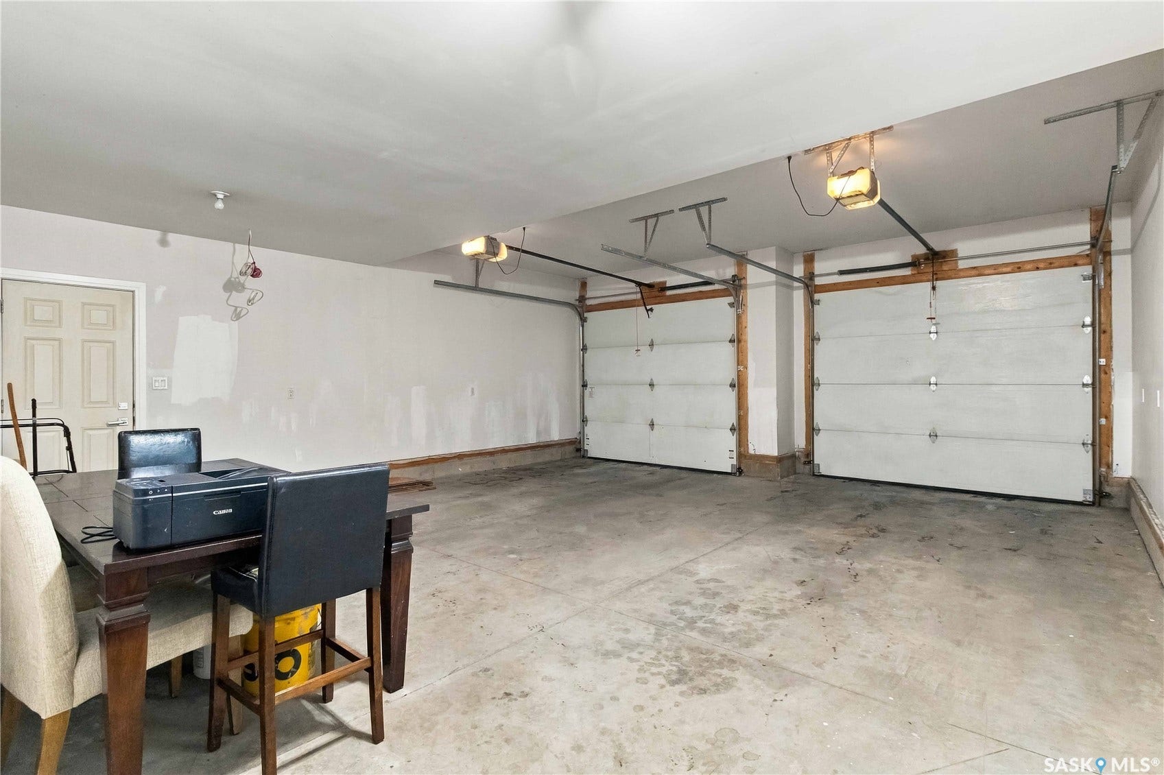 Two overhead garage doors with automatic openers, concrete flooring, and a side entry door