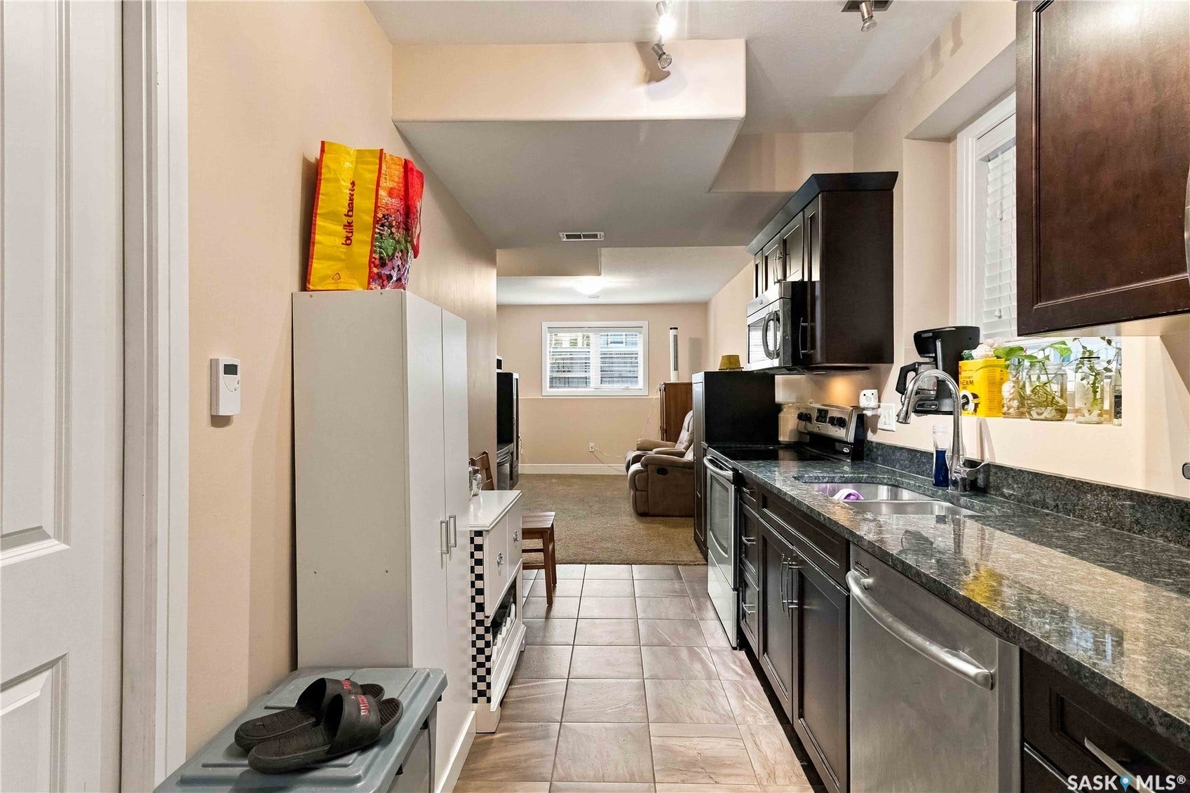 Galley kitchen with dark wood-finish cabinetry, stainless steel appliances, and stone countertops