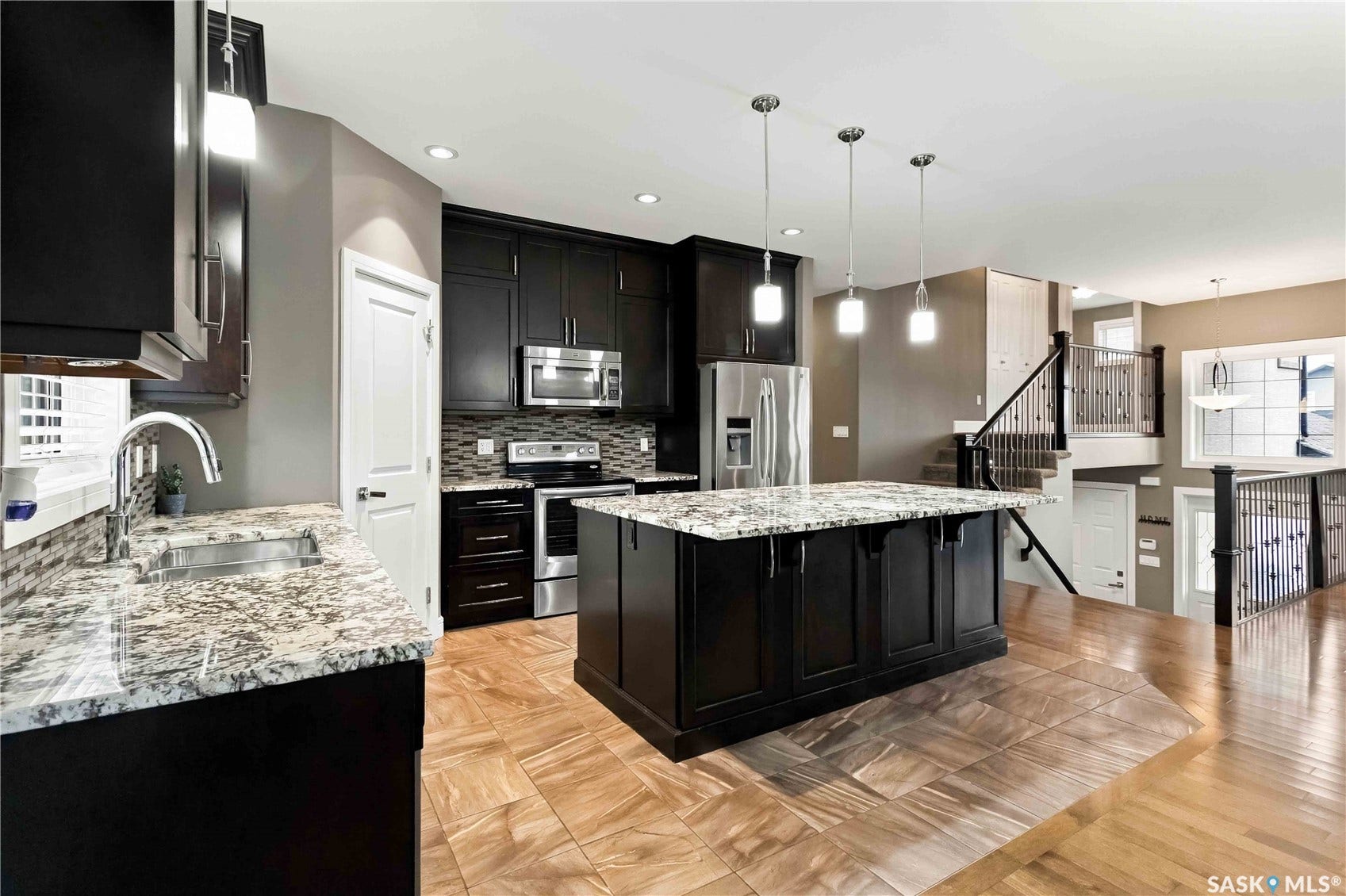 Kitchen with dark wood cabinetry, stainless steel appliances, granite countertops, and a large central island with pendant lighting