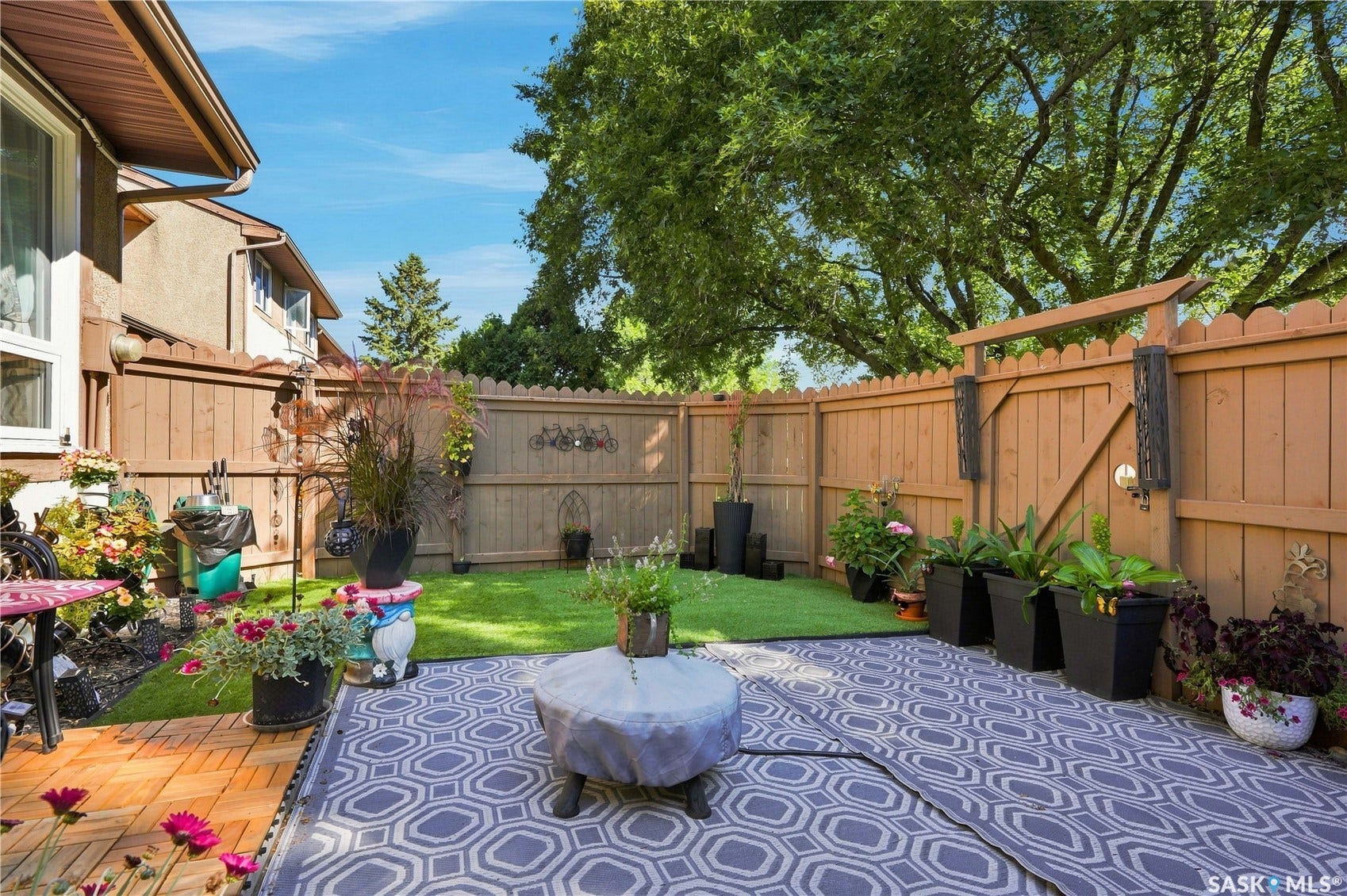 Fenced backyard featuring a mix of artificial turf and a patterned outdoor rug
