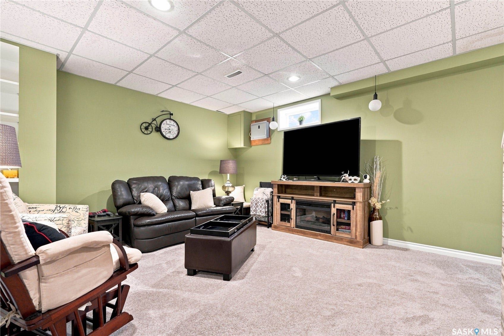 Recessed lighting, drop ceiling, carpet flooring, perimeter wall lighting, and a built-in media console with electric fireplace